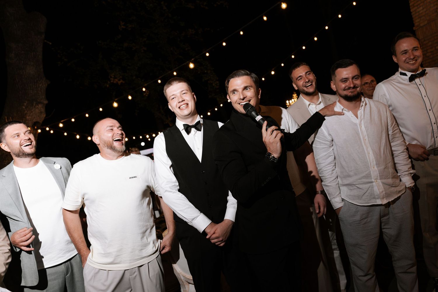 Candid nighttime celebration photo with group laughing under string lights.