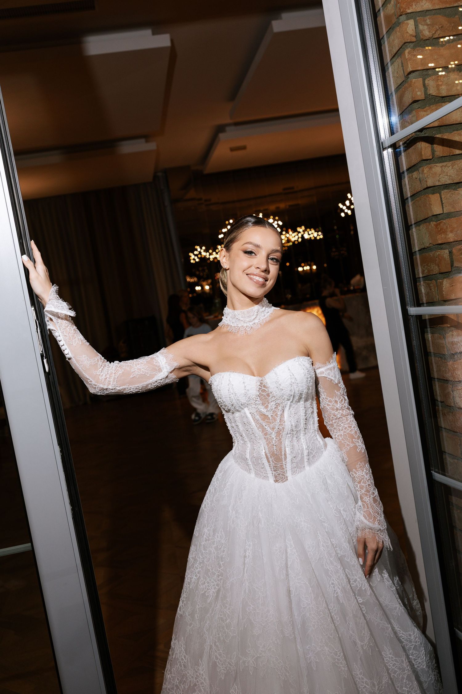 Bride in a flowing white gown twirling in front of glass doors at an indoor venue.