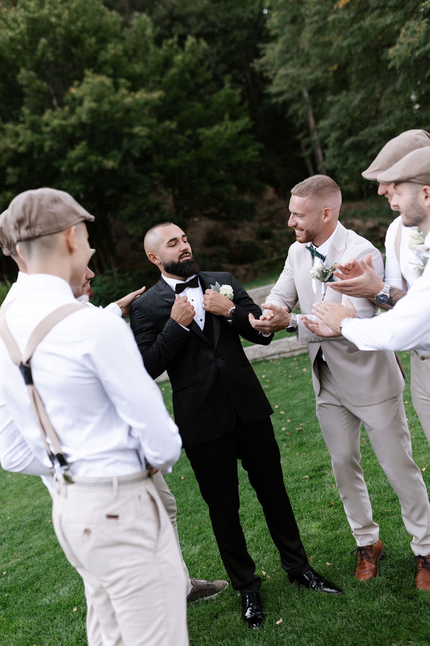 Groomsmen in white and black attire pose playfully in a line on a grassy lawn during a wedding photo session.