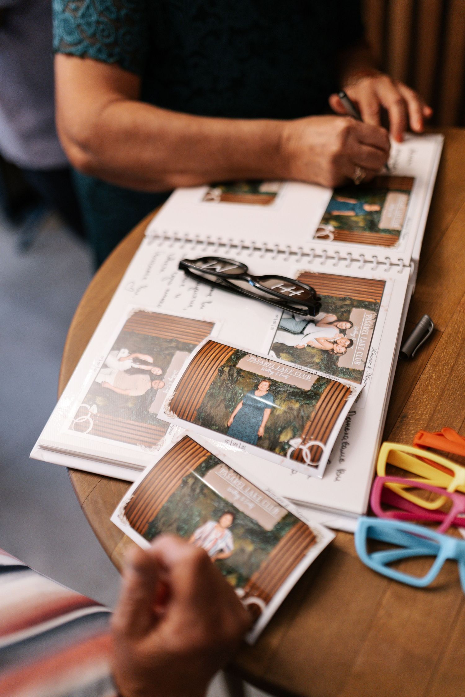 Hands flipping through pages of a photo album or scrapbook on a wooden table with colorful paper clips visible.