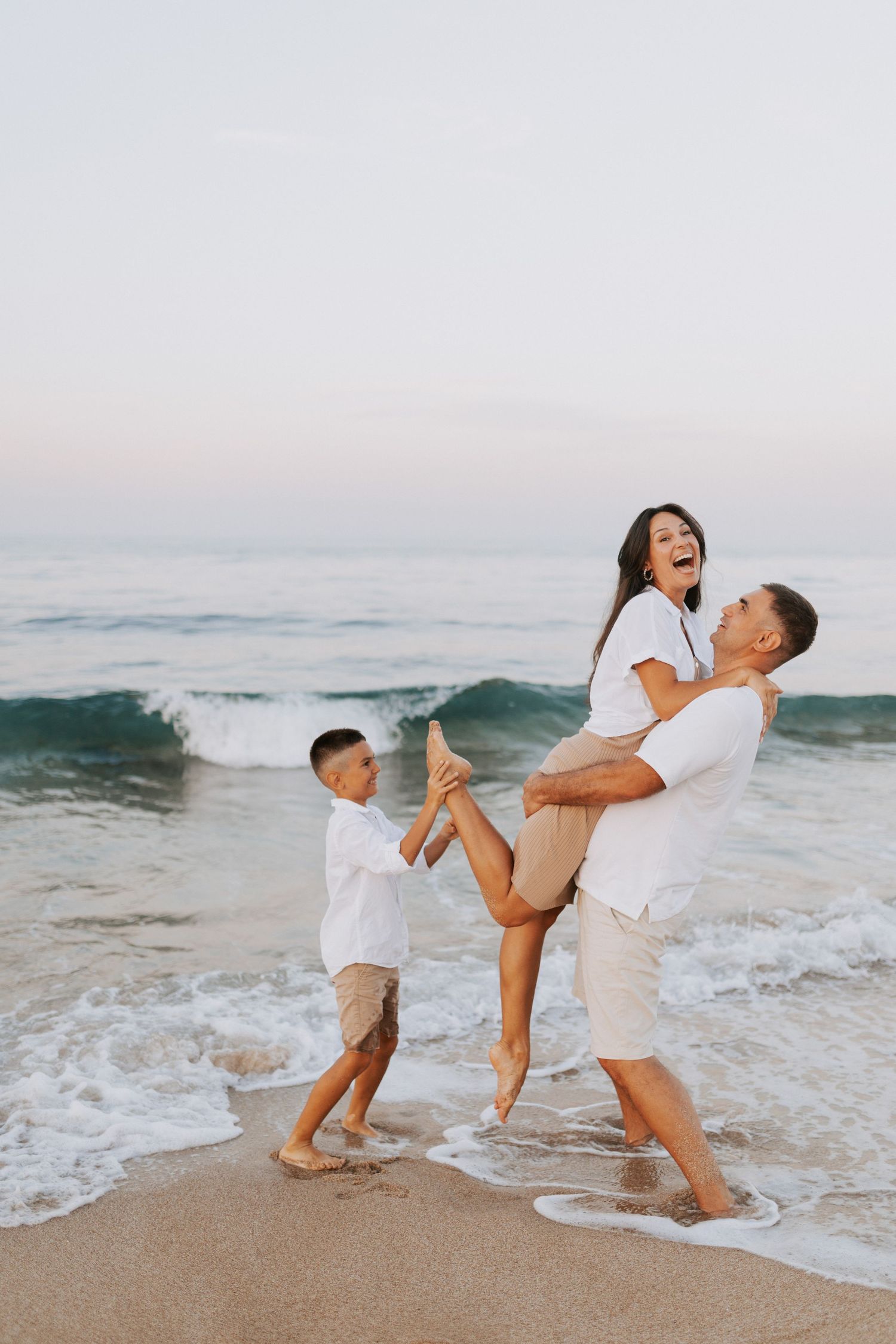 Happy family playing and laughing together on a beach at sunset with crashing waves.