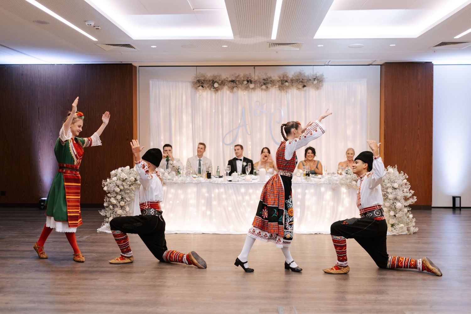 Folk dancers in traditional costumes performing choreographed routine at wedding reception.