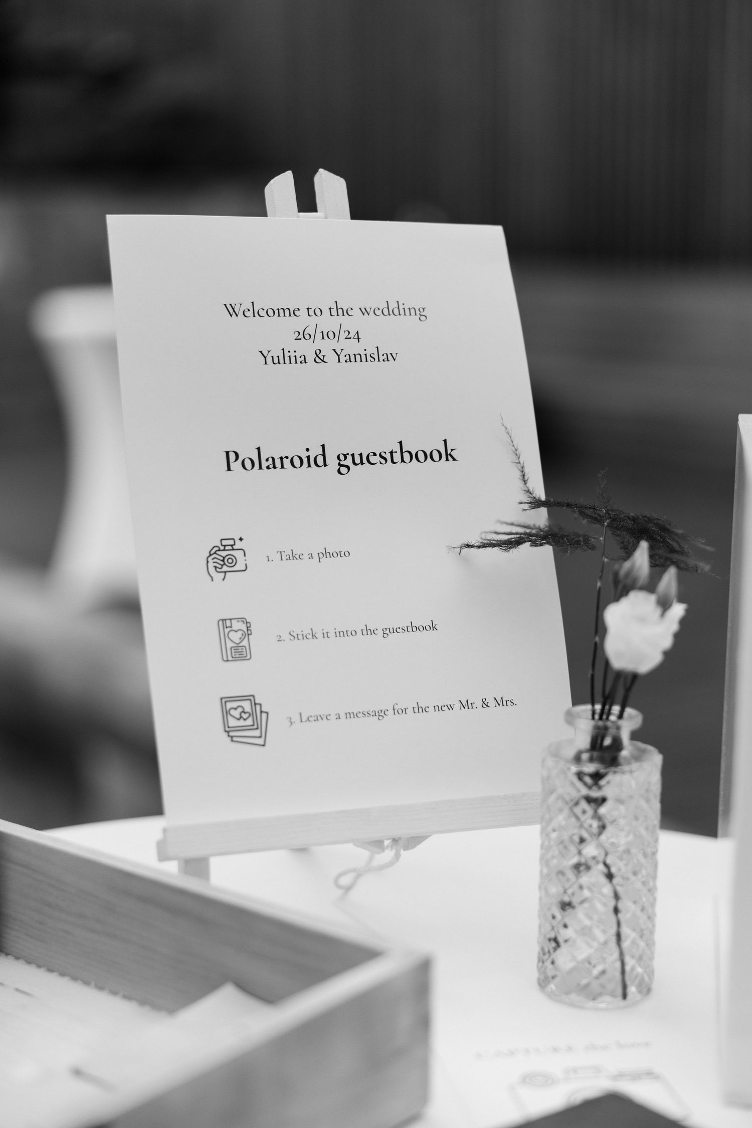 Wedding Polaroid guestbook instructions displayed on white stand with decorative vase.