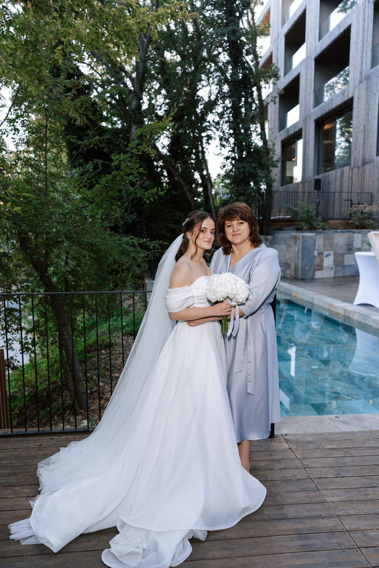 Wedding party members posing by pool at modern venue with architectural backdrop.