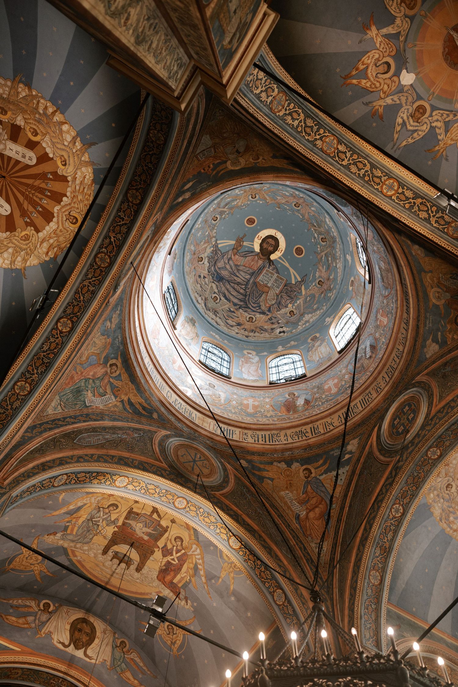 Ornate church dome with detailed religious frescoes and golden chandelier.
