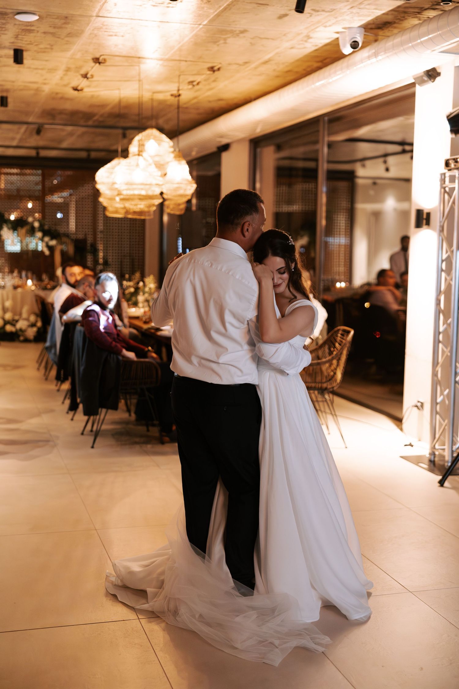 A couple shares an intimate slow dance moment in an elegantly lit reception venue.