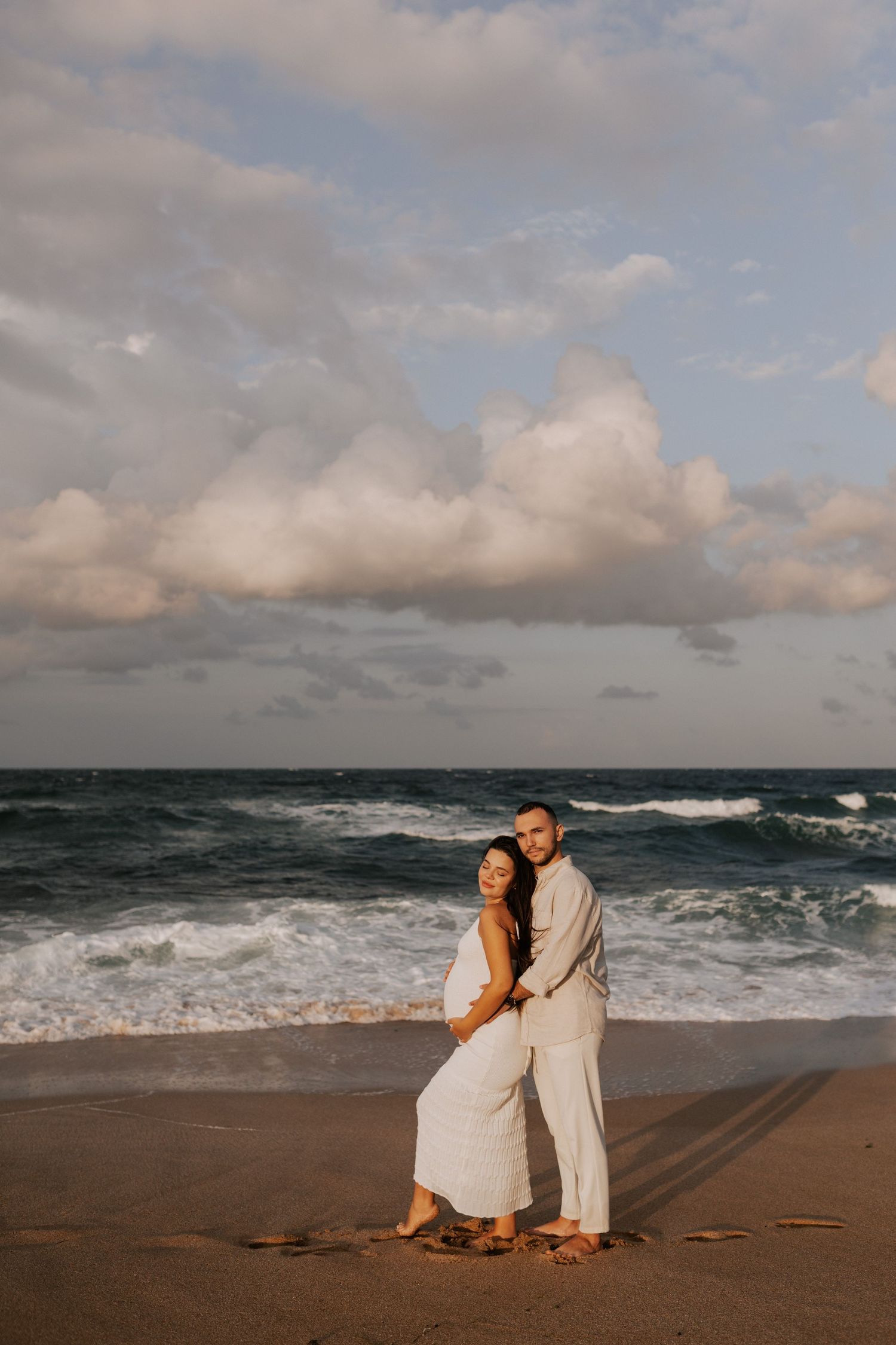 A romantic beach photoshoot with dramatic clouds and ocean waves in the background.