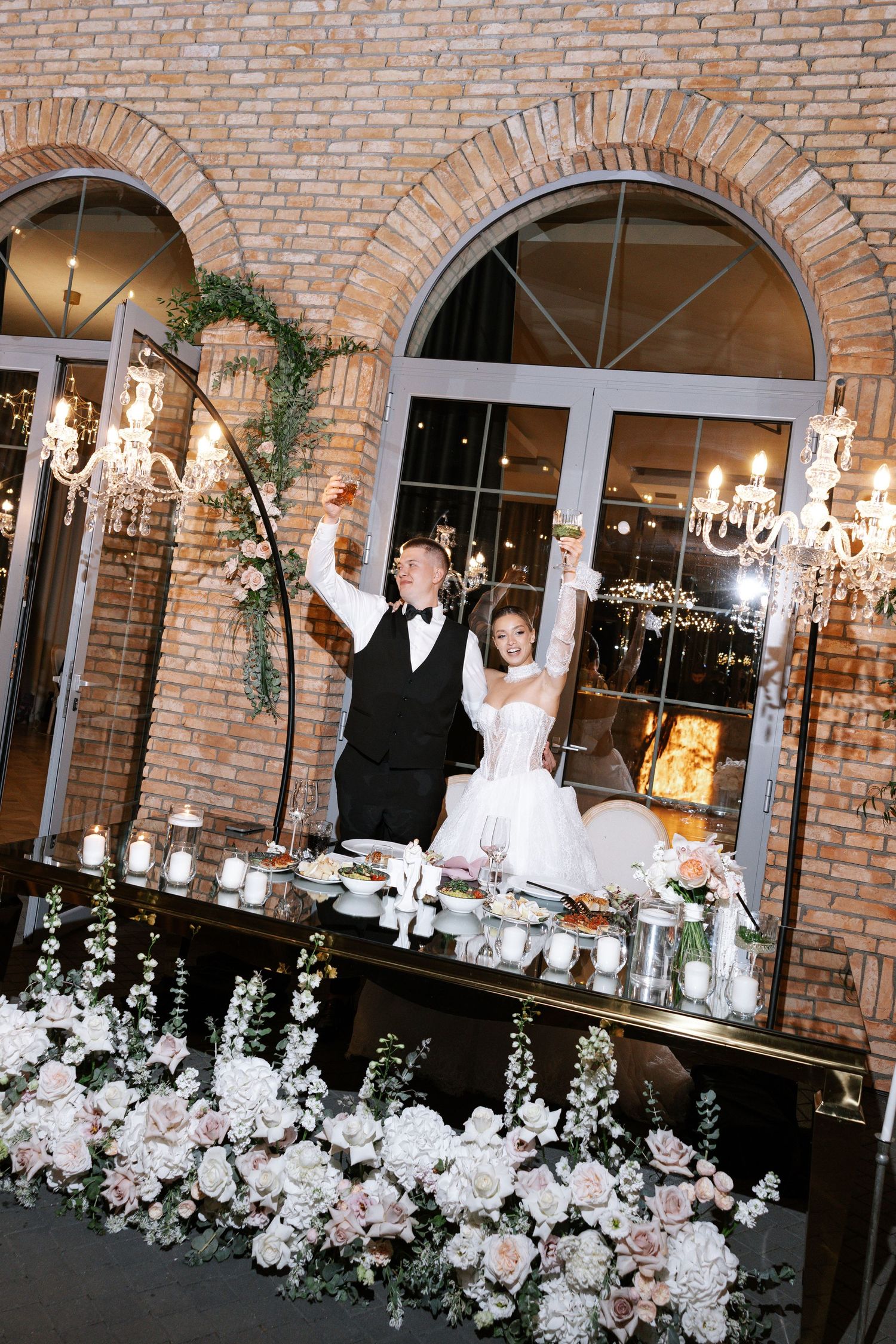 Wedding venue decorated with white floral arrangements and crystal chandeliers against brick walls.