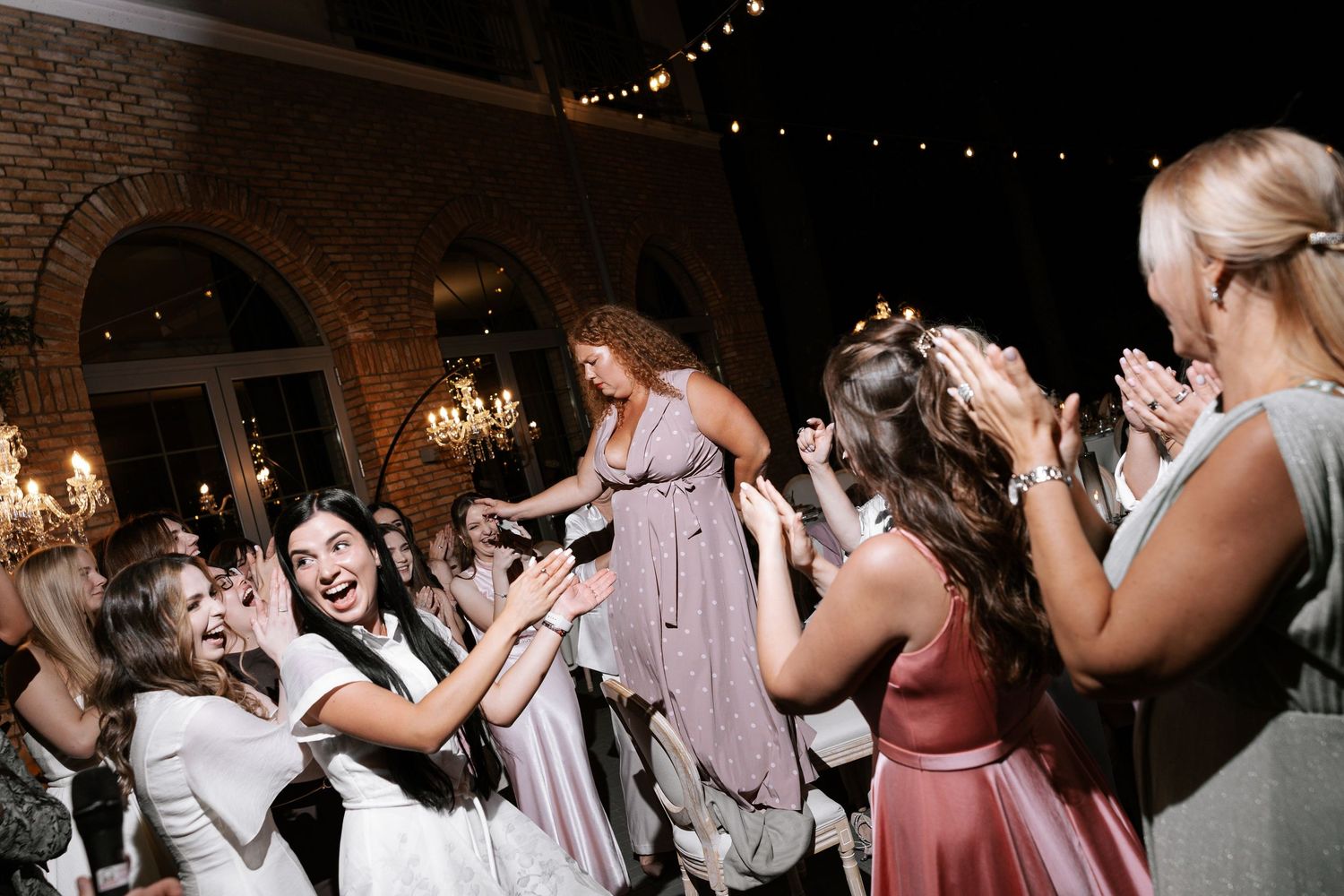 Guests dancing and celebrating at a wedding reception in an elegant brick-walled venue with chandeliers.