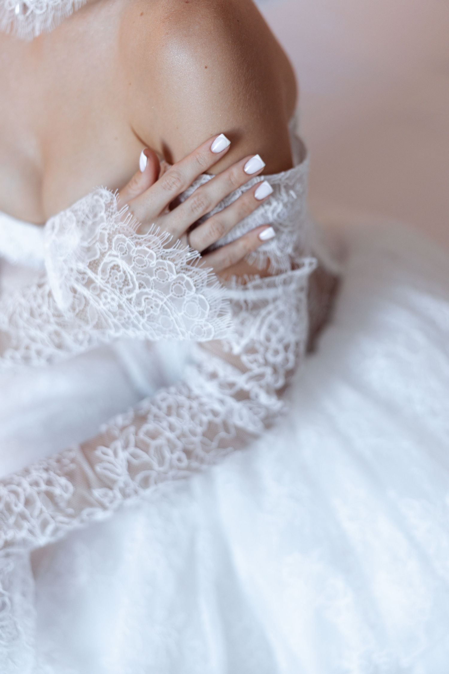 Close-up of white manicured nails and delicate lace detail on wedding dress.
