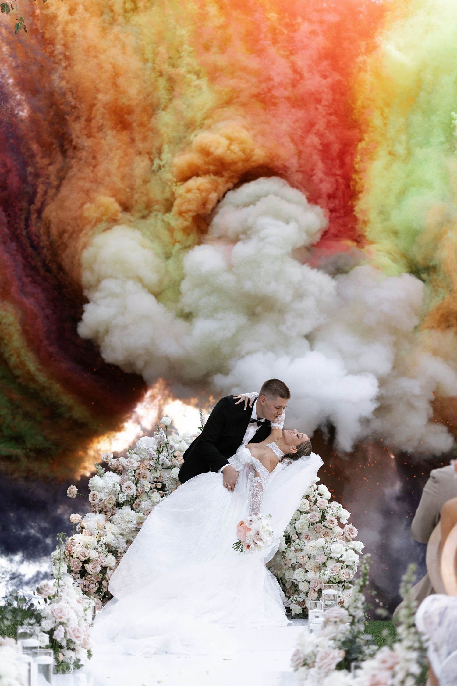 Artistic wedding photo with colorful smoke bombs creating a dramatic orange and red backdrop behind the couple.