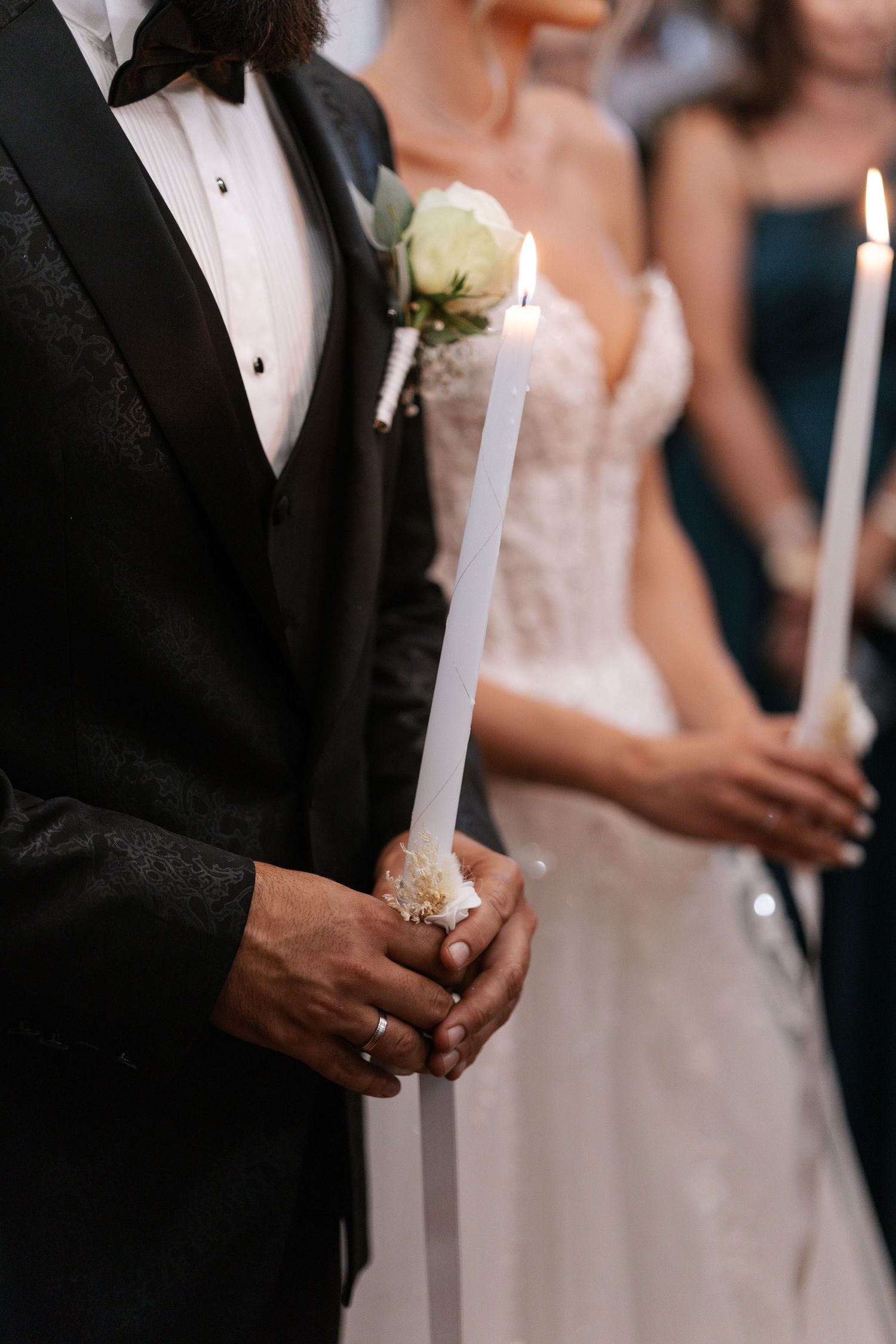 Wedding ceremony guests in formal attire hold lit white candles during a traditional unity candle lighting ritual.
