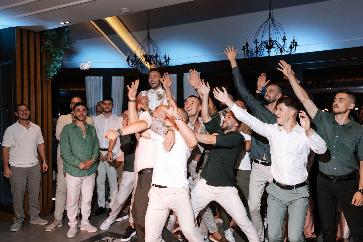 People dancing and celebrating at a wedding reception with arms raised on the dance floor.