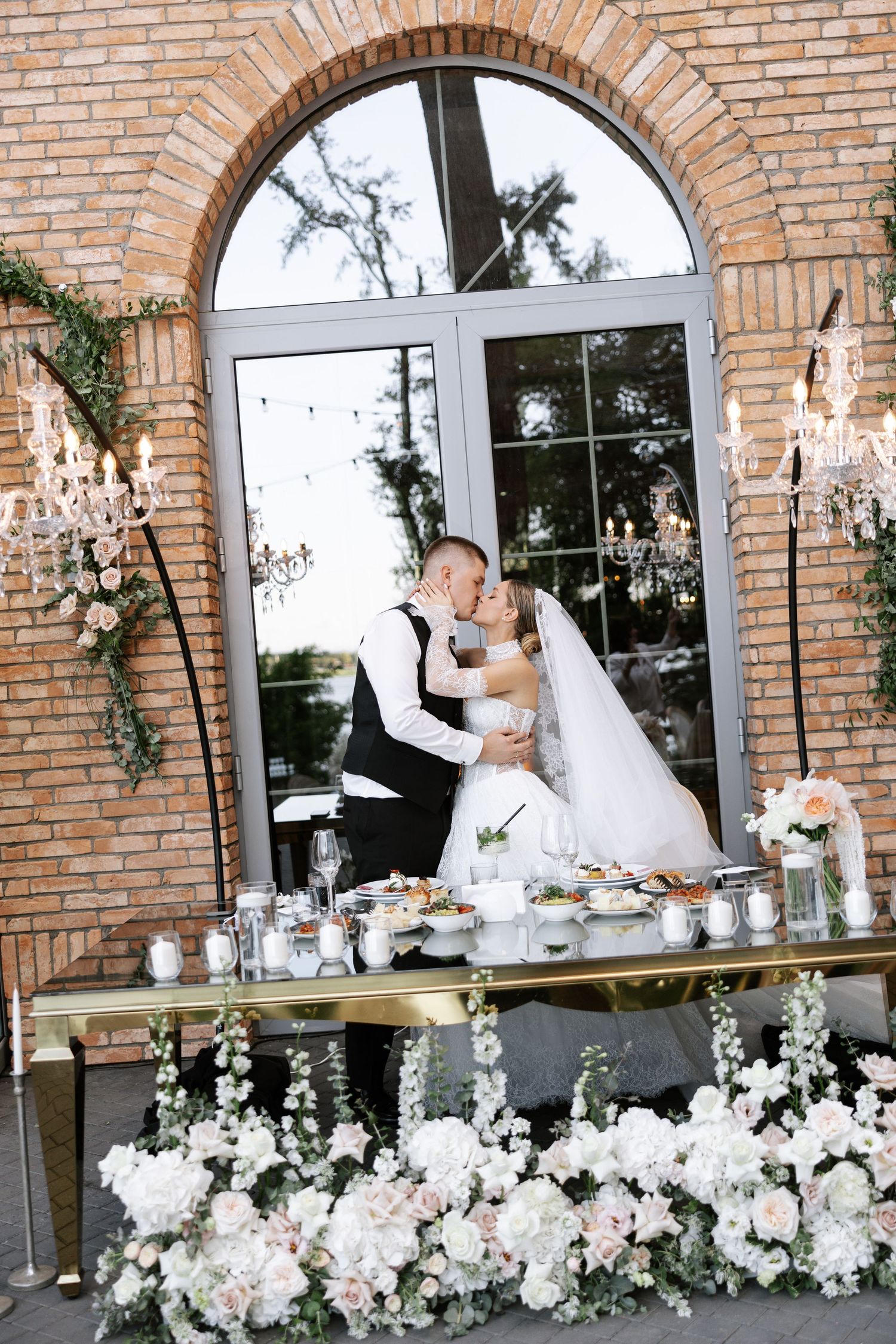 Wedding reception table decorated with elegant white floral arrangements against brick archways.