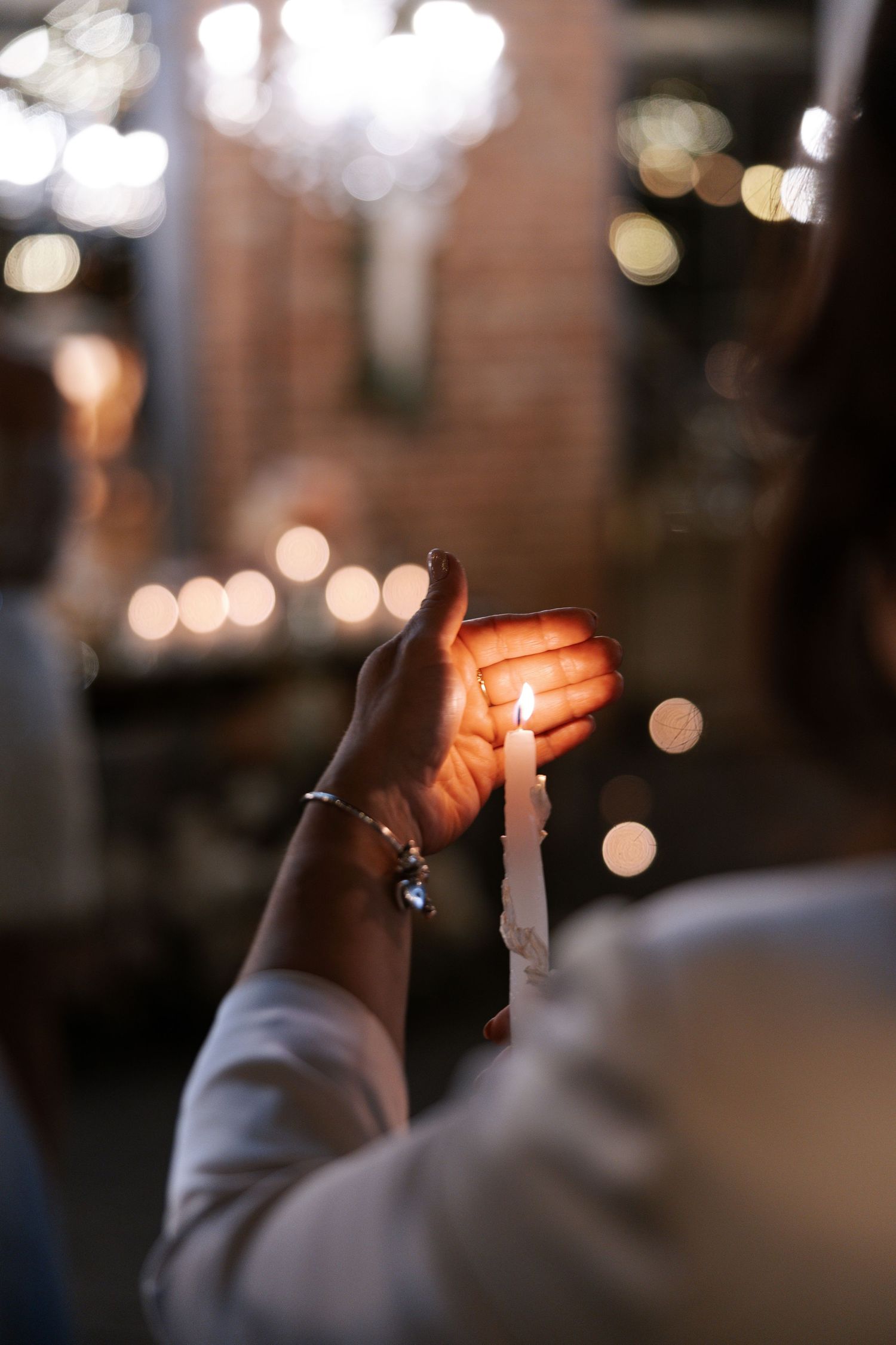 Atmospheric photo of hands holding lit candles during an evening wedding ceremony.
