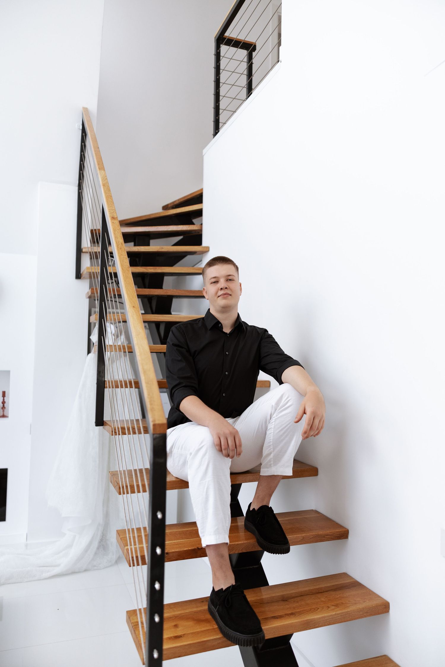 Modern wooden staircase with black metal railings in a minimalist white interior.