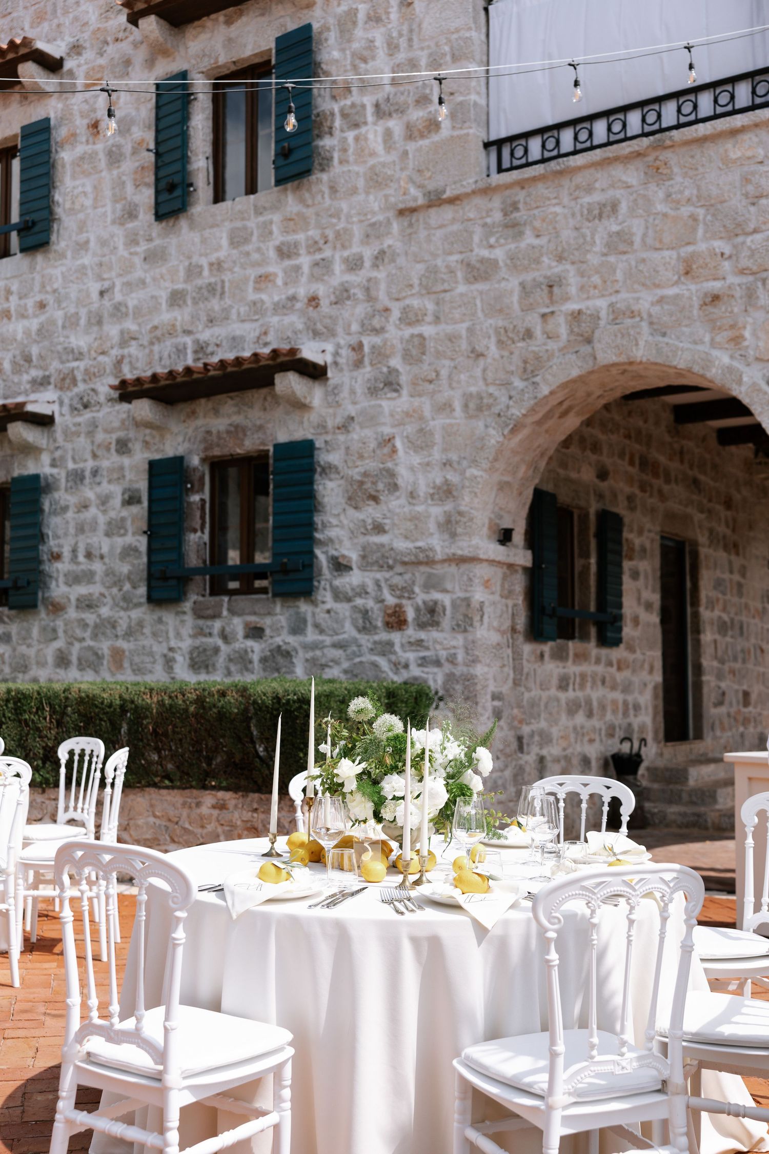 Elegant outdoor wedding reception setup with white tables and chairs against a rustic stone building facade.