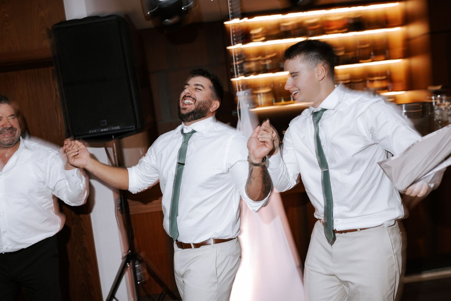 Guests in white dress shirts and green ties dance enthusiastically at a wedding reception.