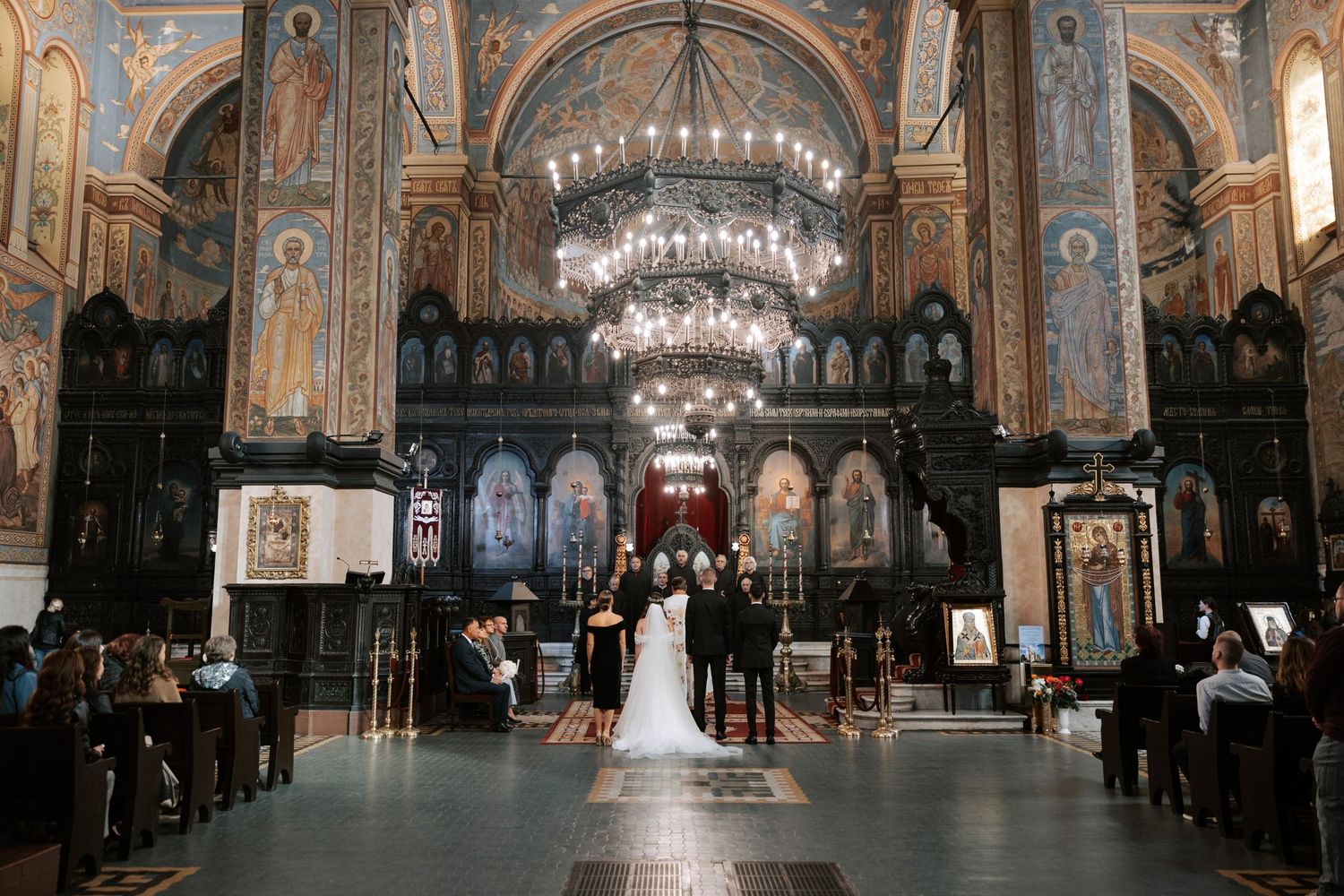 Grand orthodox church interior with crystal chandeliers during wedding ceremony.