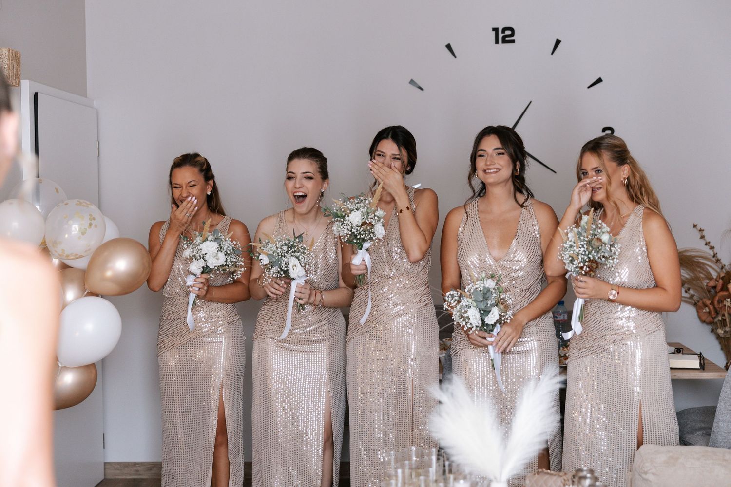 Bridesmaids in matching sparkly champagne sequin dresses laugh together while holding bouquets at a wedding celebration.
