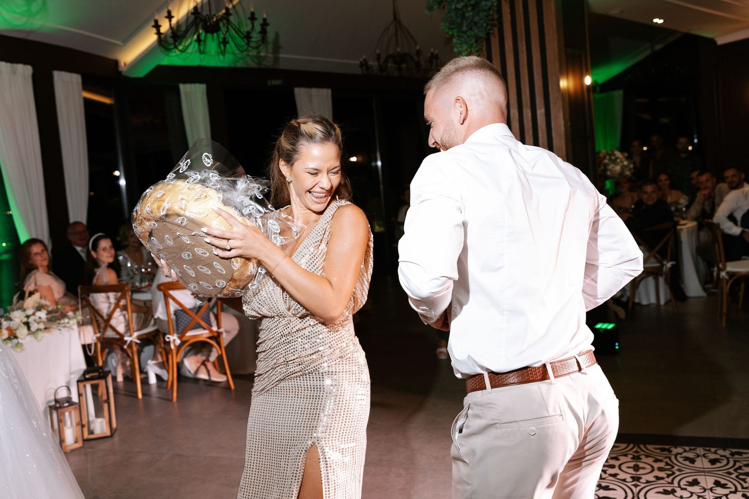 People dancing and celebrating at a wedding reception with green lighting and white decor in a banquet hall.