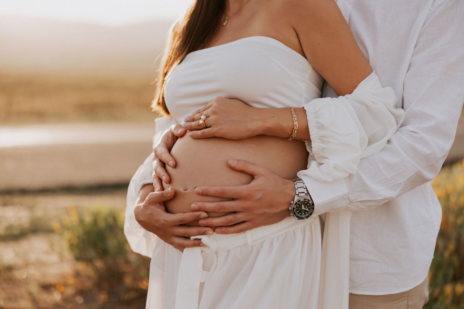 Close-up of couple's hands cradling baby bump during outdoor maternity session.