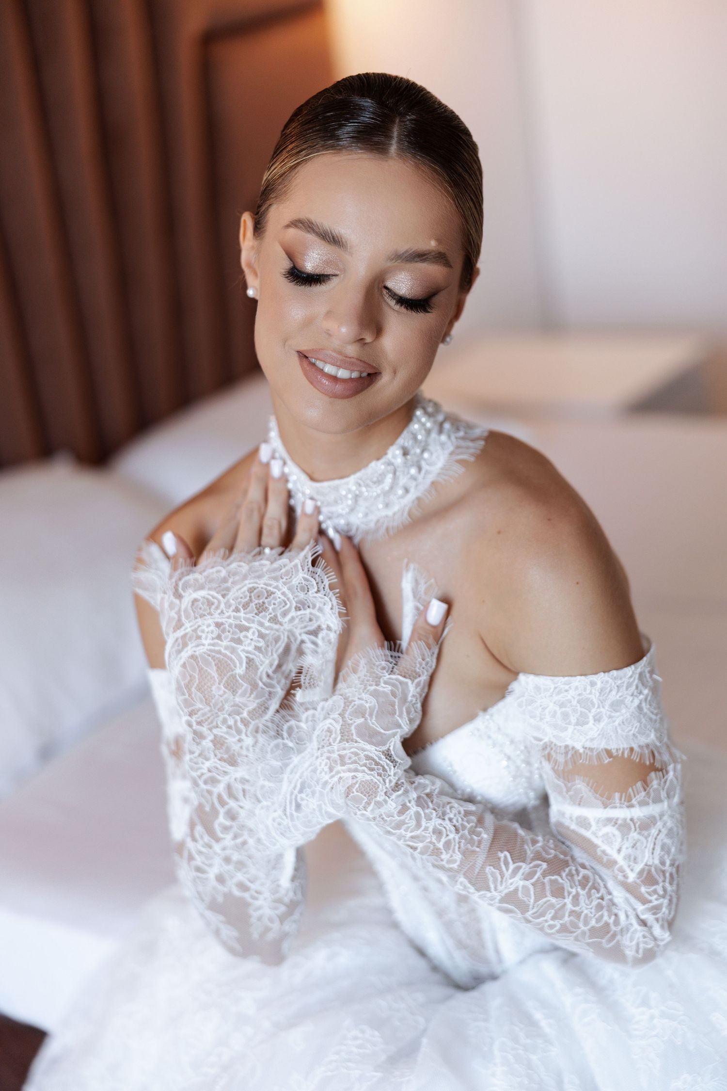 Beautiful bride in delicate white lace wedding dress with off-shoulder sleeves smiles with eyes closed.