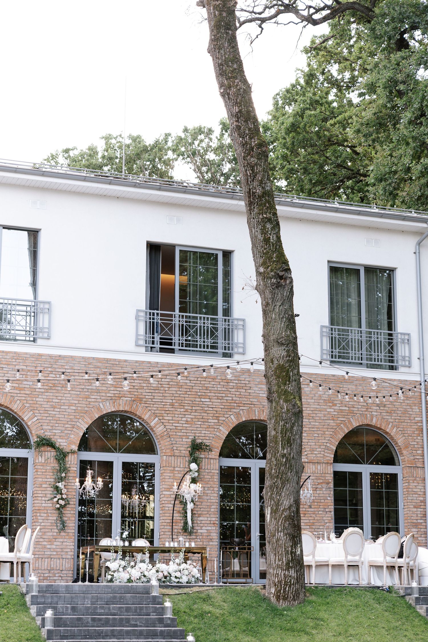 Elegant white wedding venue with brick arches, string lights and outdoor seating setup.