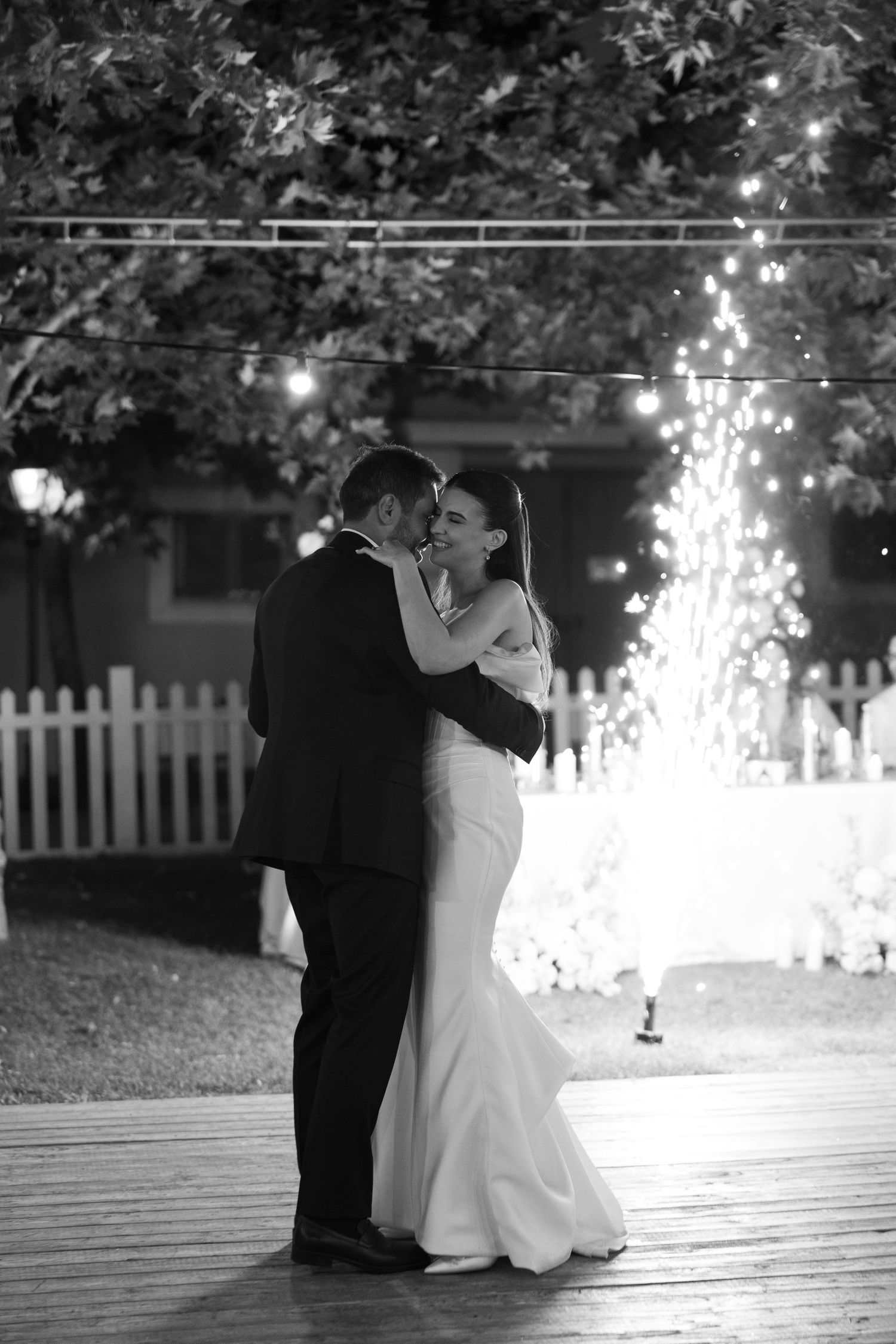 A romantic black and white wedding photo sequence showing a couple sitting on wooden decking with sparklers in the background.