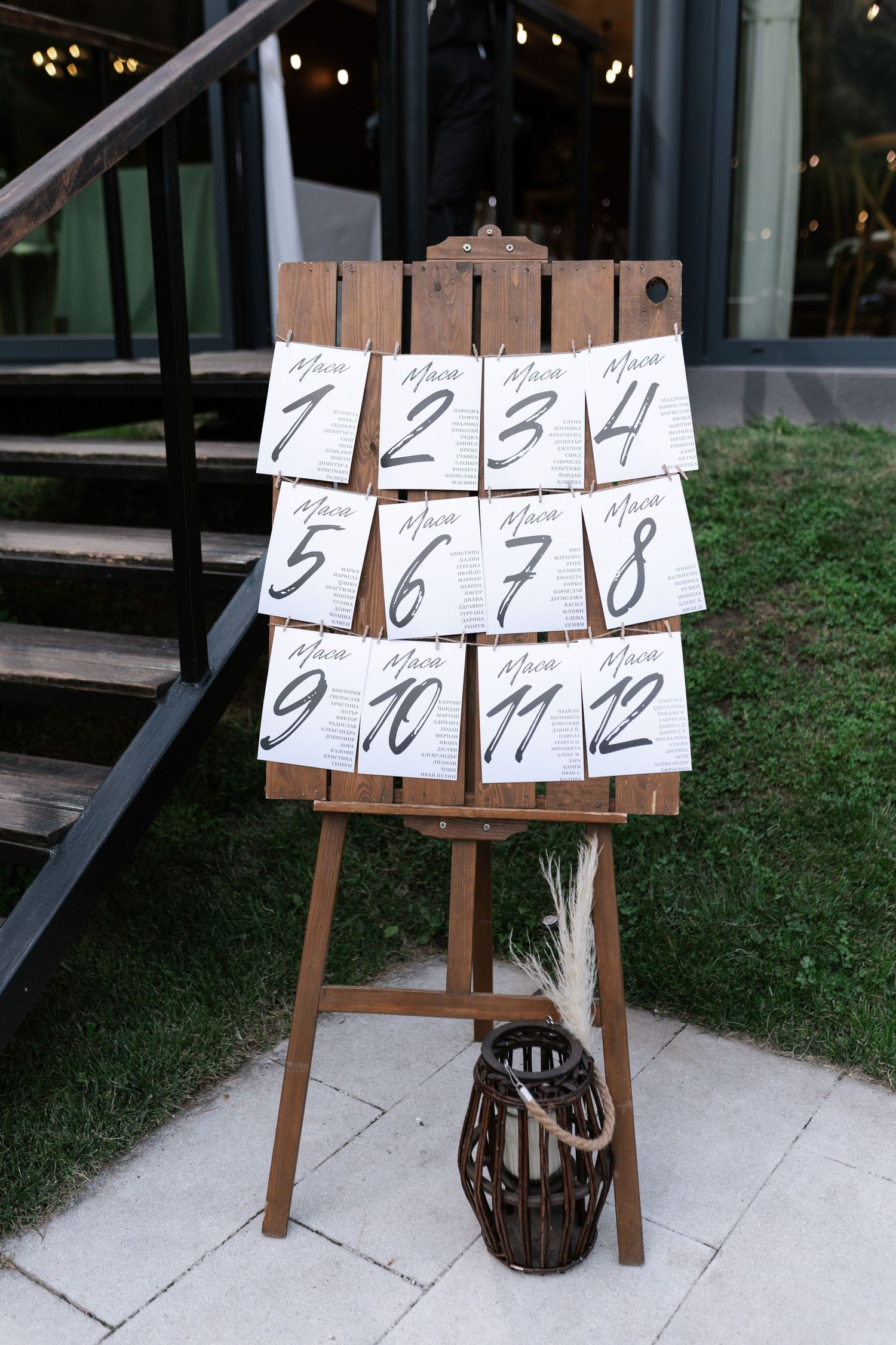 A rustic wooden table number display with numbers 1-12 mounted on boards, with a decorative lantern at the base.