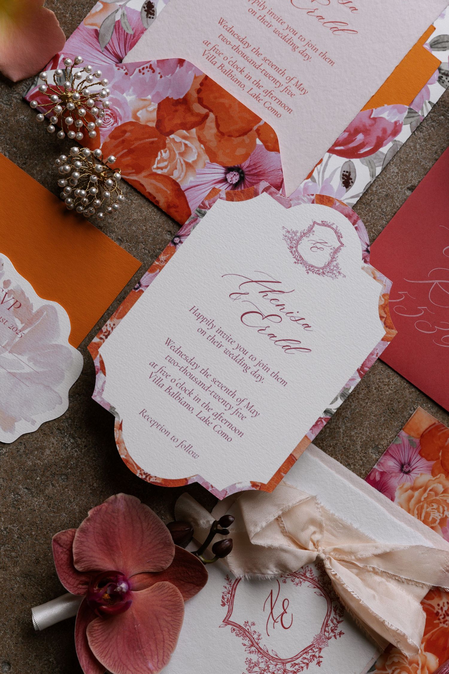 Elegant wedding invitation suite with floral designs in coral and pink tones, featuring ornate text and pearl accents.
