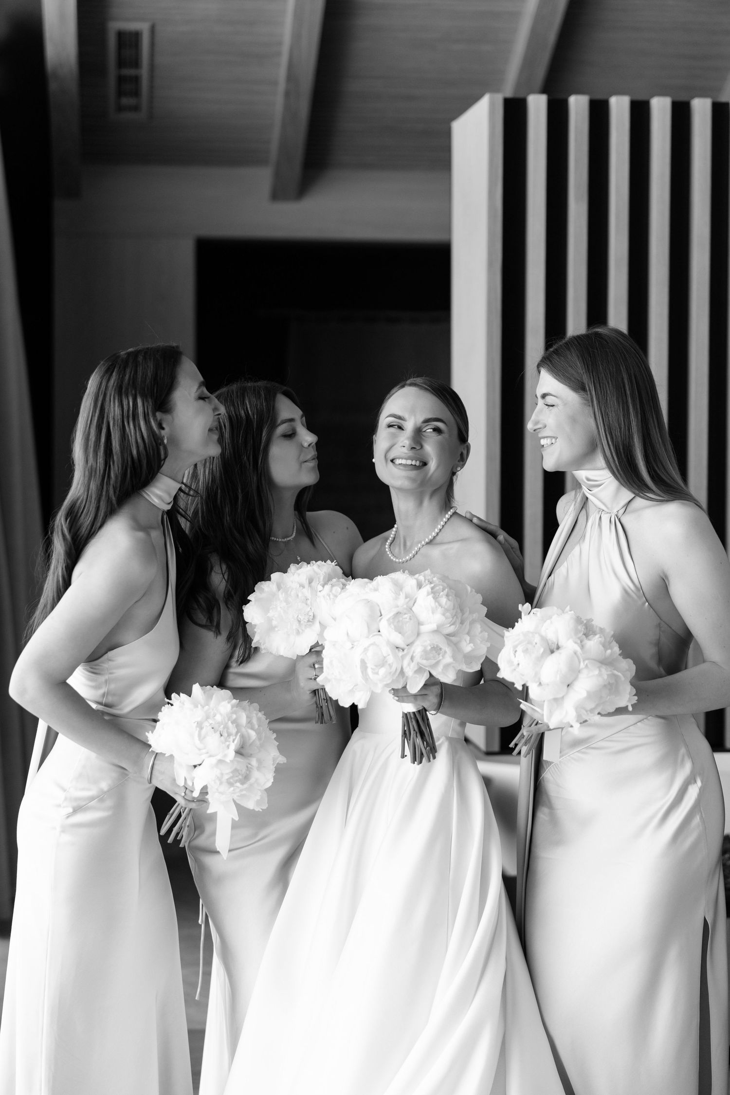 A line of bridesmaids in white dresses with ruffled necklines stand together in a row at a wedding.