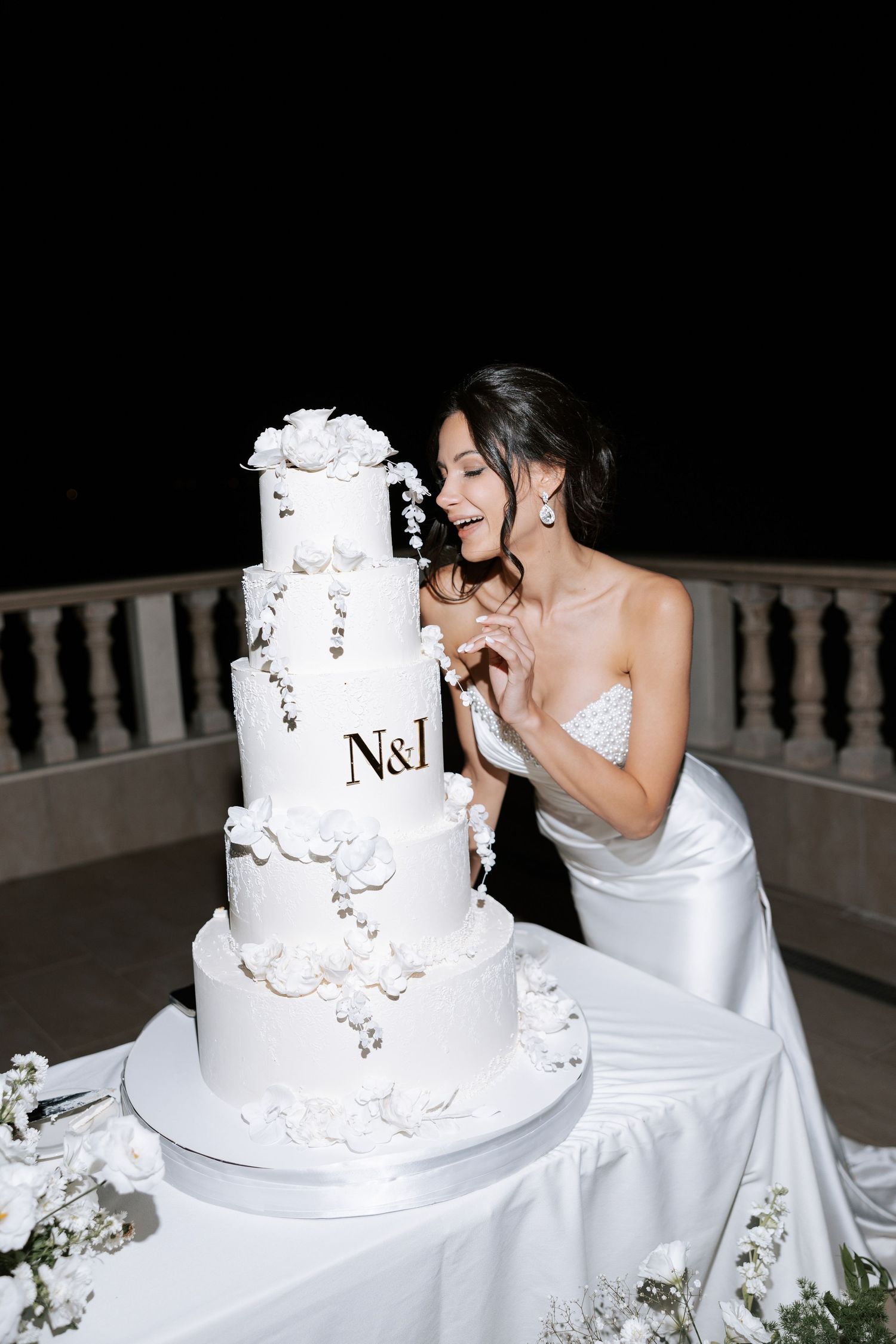 Elegant white tiered wedding cake with floral decorations displayed on outdoor balcony.