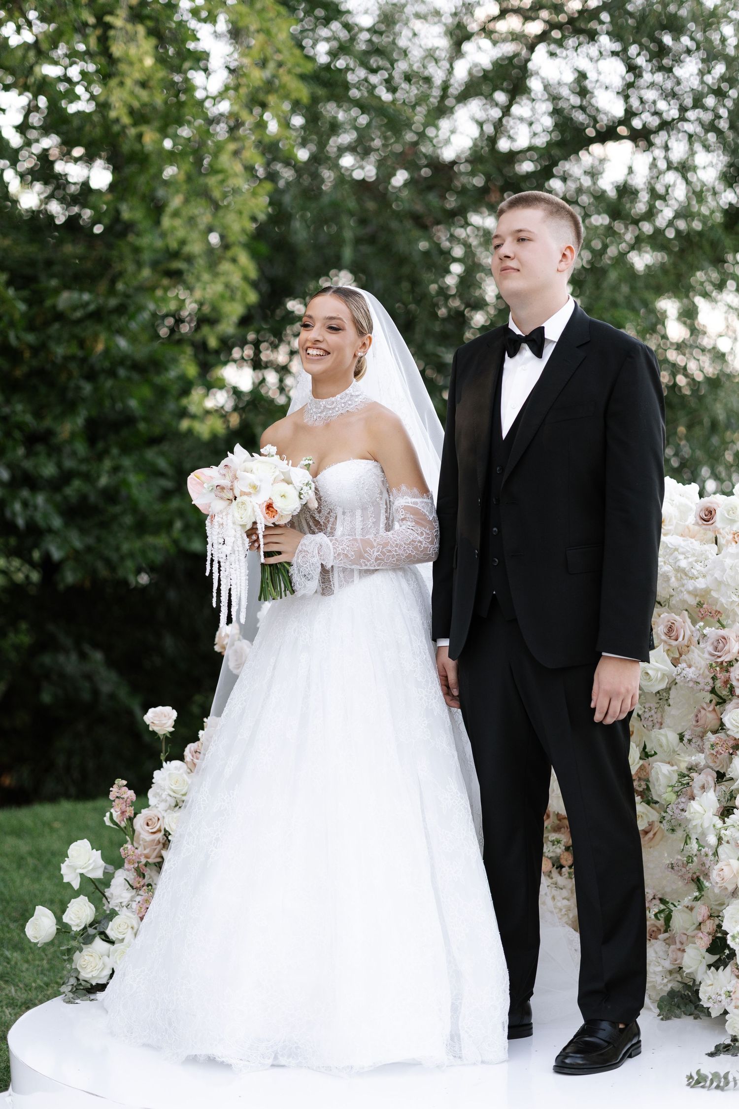 Wedding couple posing by floral arch decorations in an outdoor garden setting.