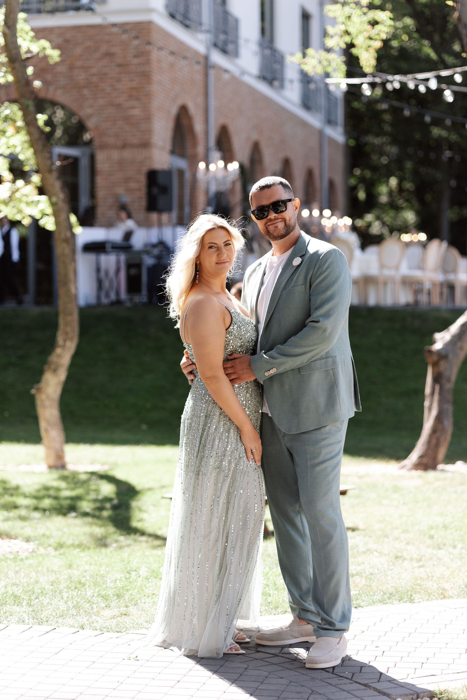Elegant couple poses at outdoor wedding venue with brick archways and string lights.