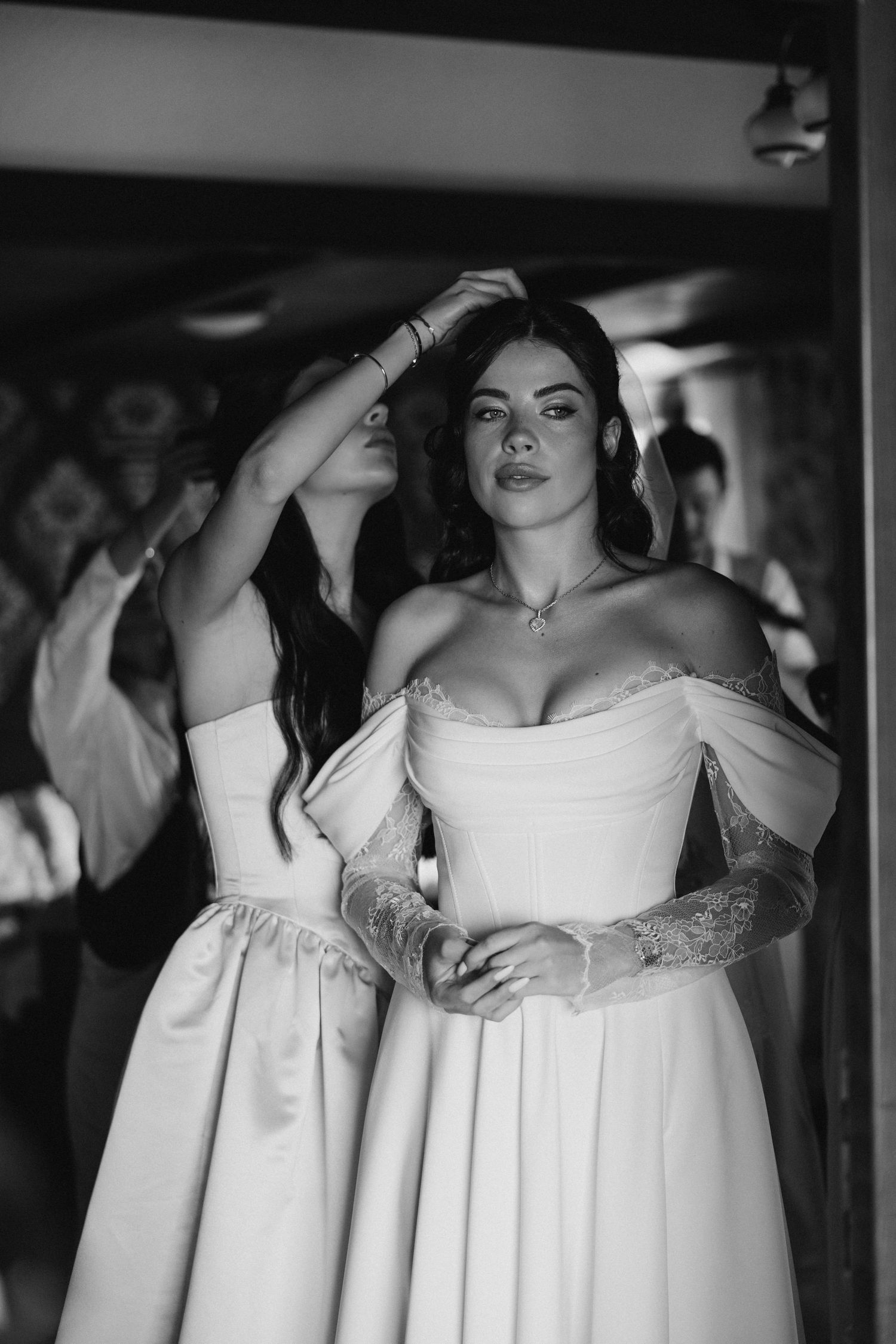 Black and white photo of a woman in an elegant off-shoulder white wedding gown with long sleeves and fitted bodice.