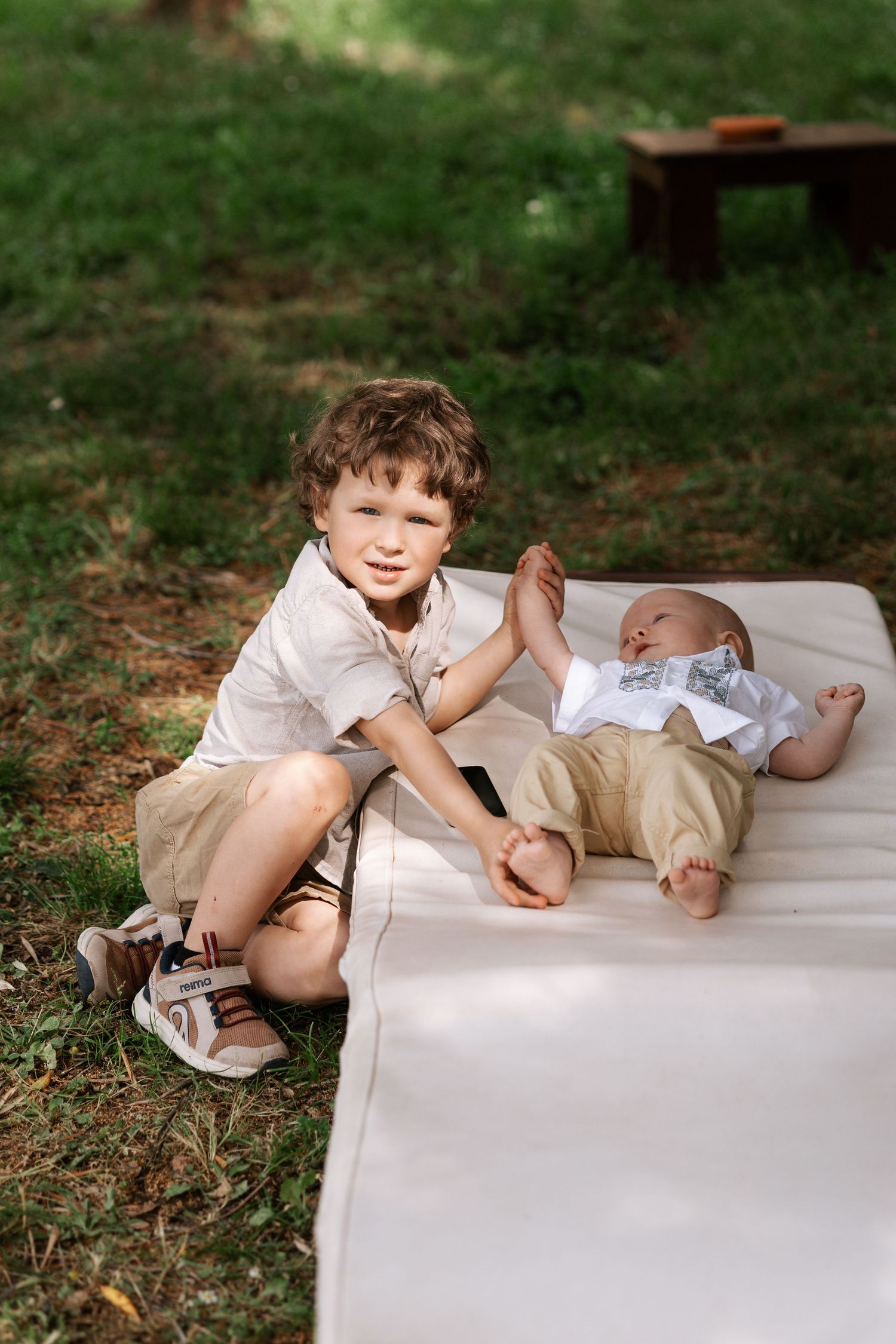 Two children play together on a white blanket outdoors in a series of candid moments.