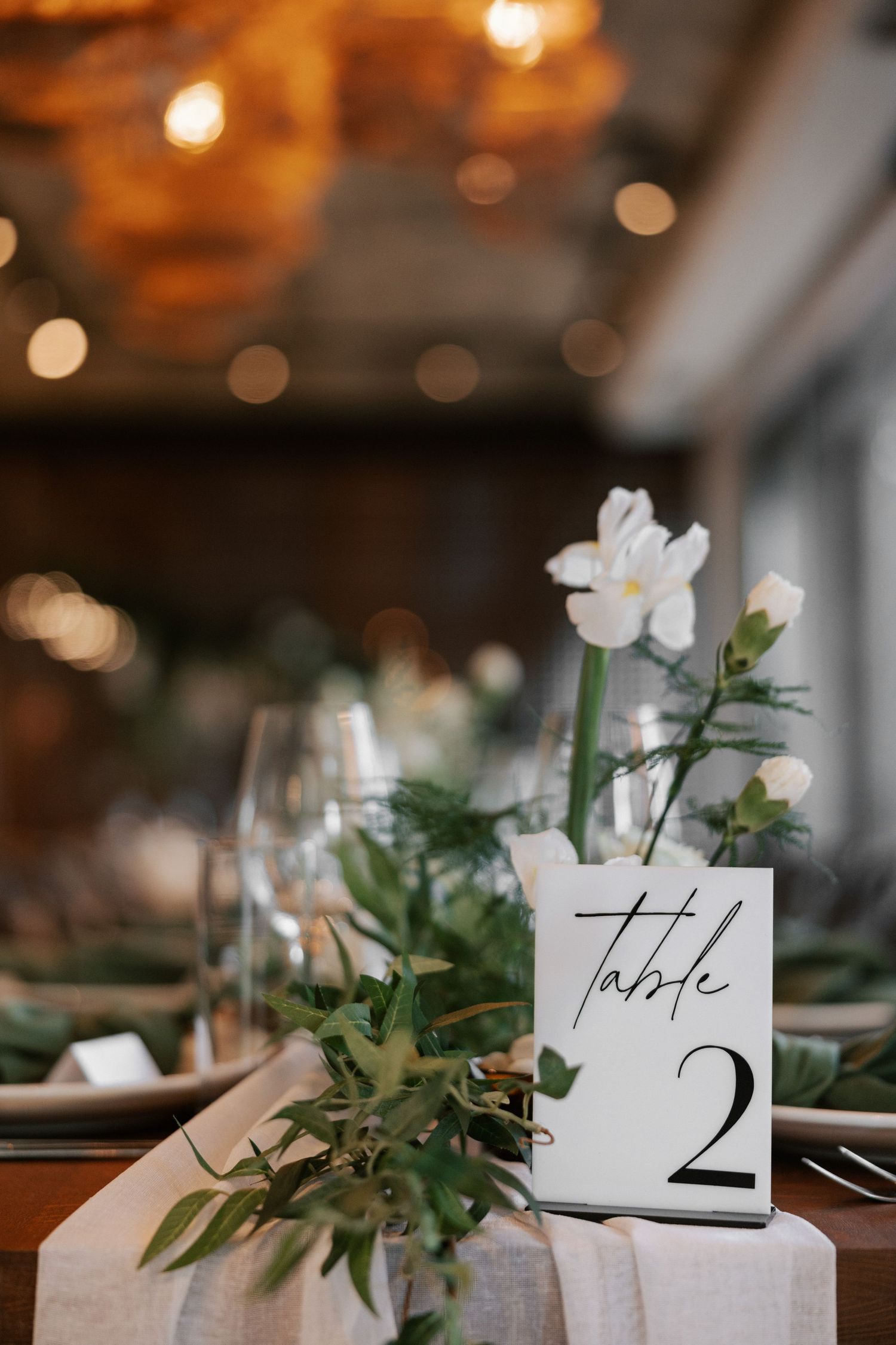 Elegant table setting with a white flower centerpiece and modern table number card.