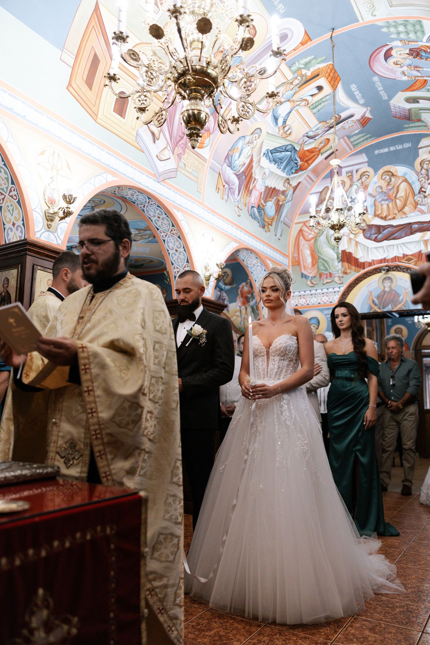 Orthodox Christian wedding ceremony taking place inside ornate church with beautifully painted ceiling and icons.