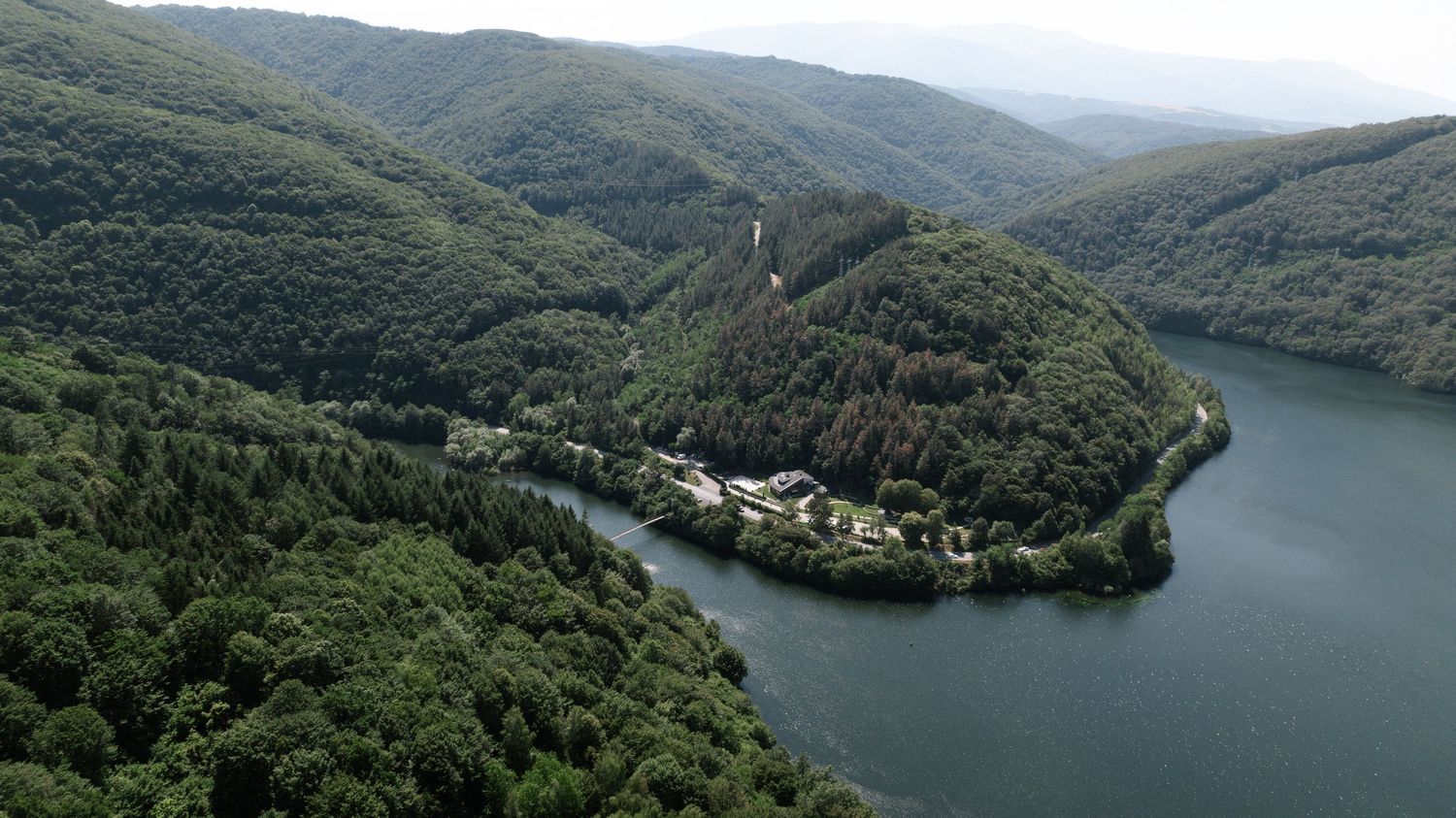 Aerial view of a scenic river bend surrounded by forested mountains with a small village nestled along the shore.