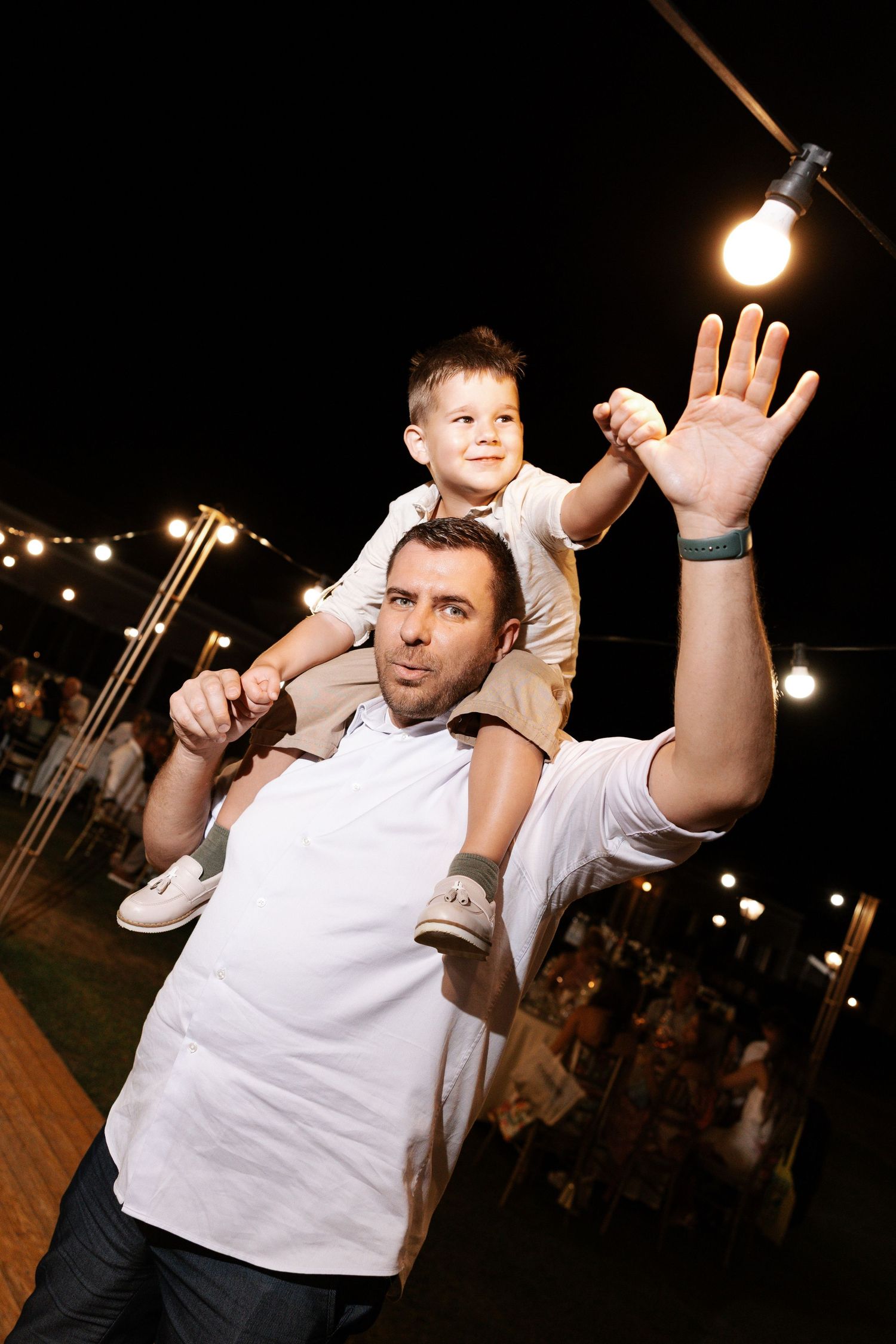 People in white shirts dancing energetically at a nighttime event with string lights overhead.