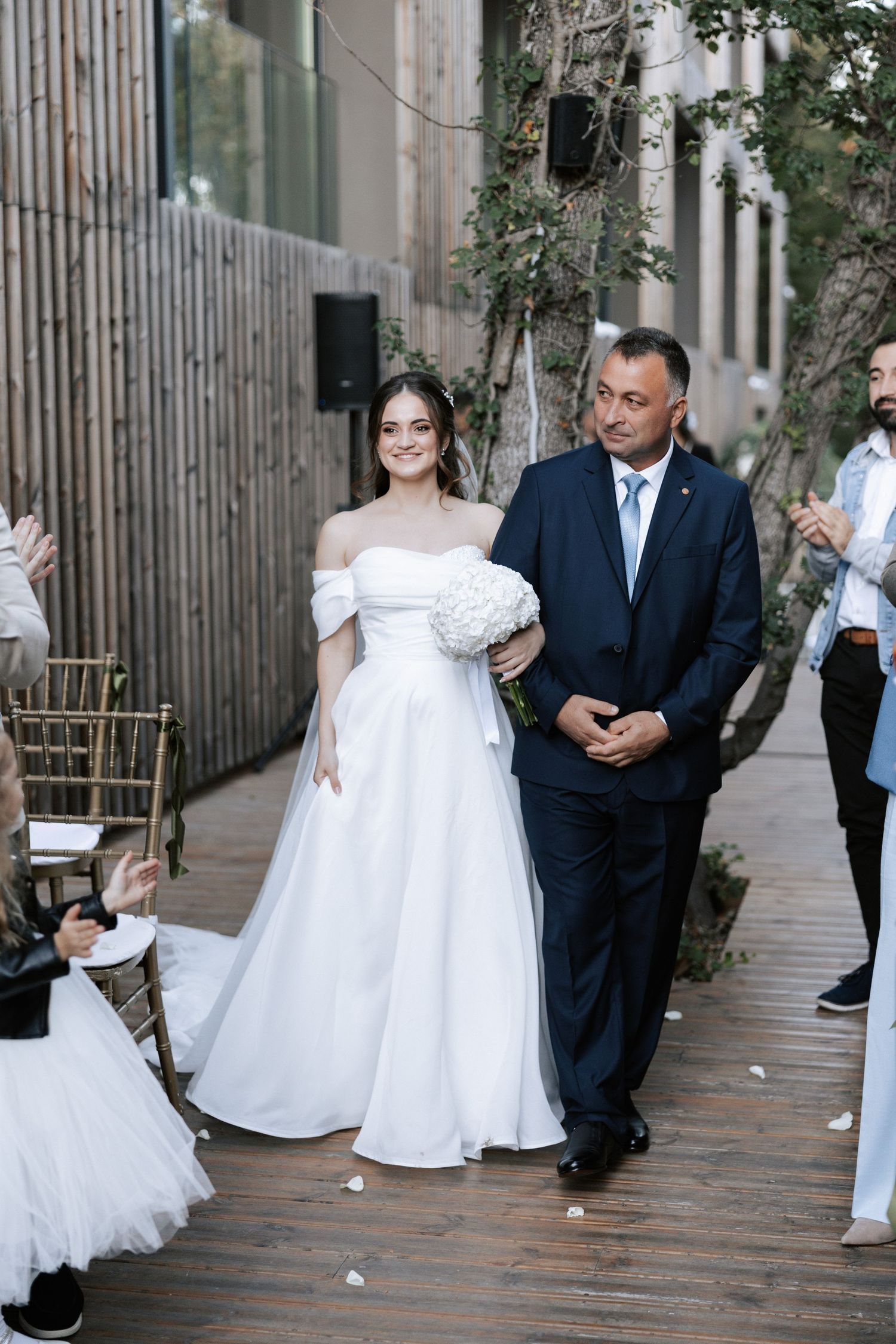 A traditional wedding processional on a wooden deck with natural forest backdrop.
