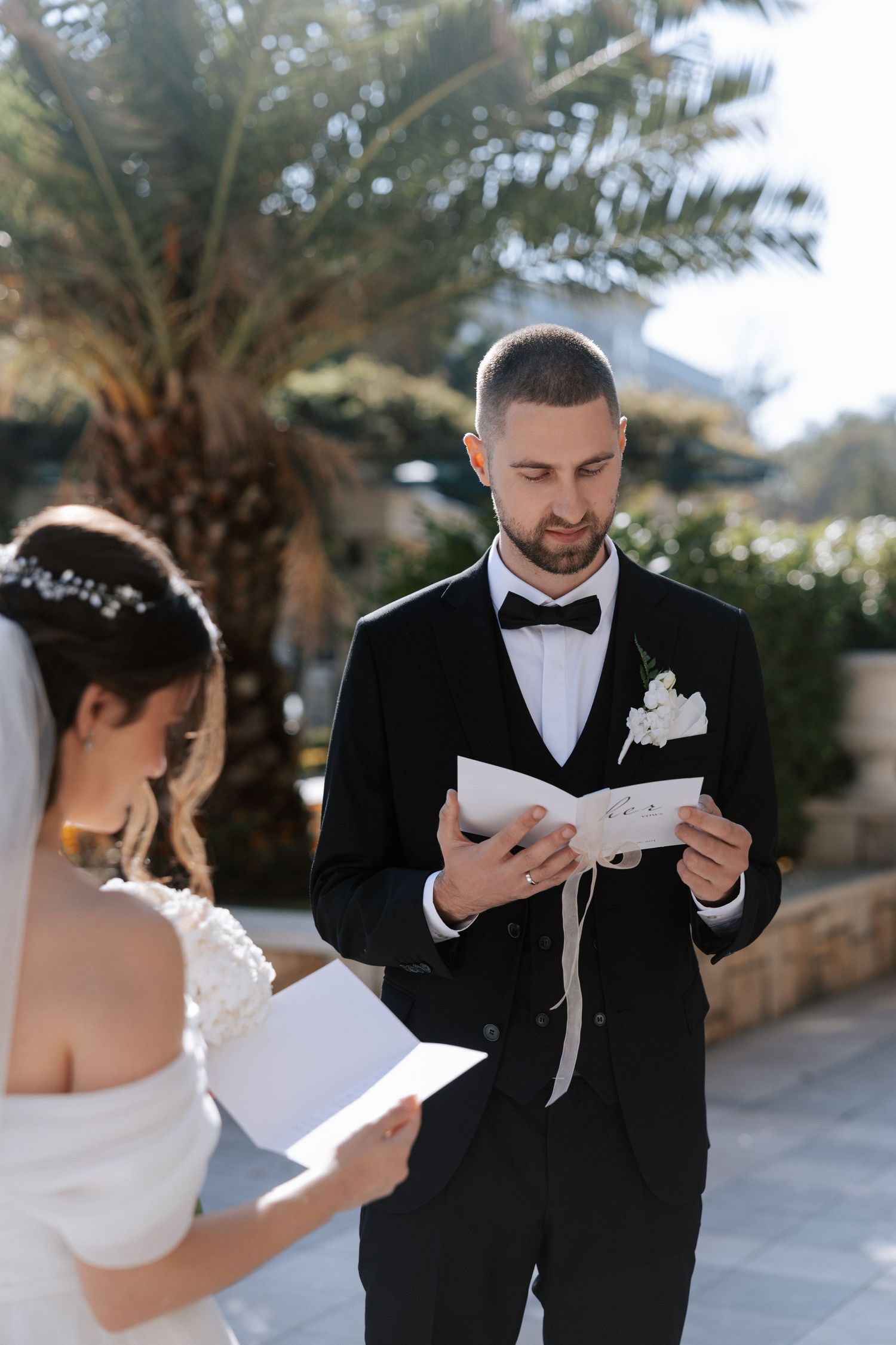 A couple exchanging personal wedding vows outdoors with a palm tree in the background.