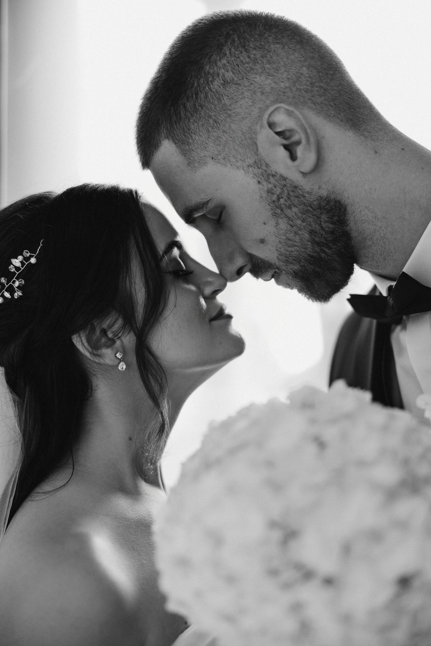 Intimate black and white portrait of newlyweds sharing a romantic moment with foreheads touching.