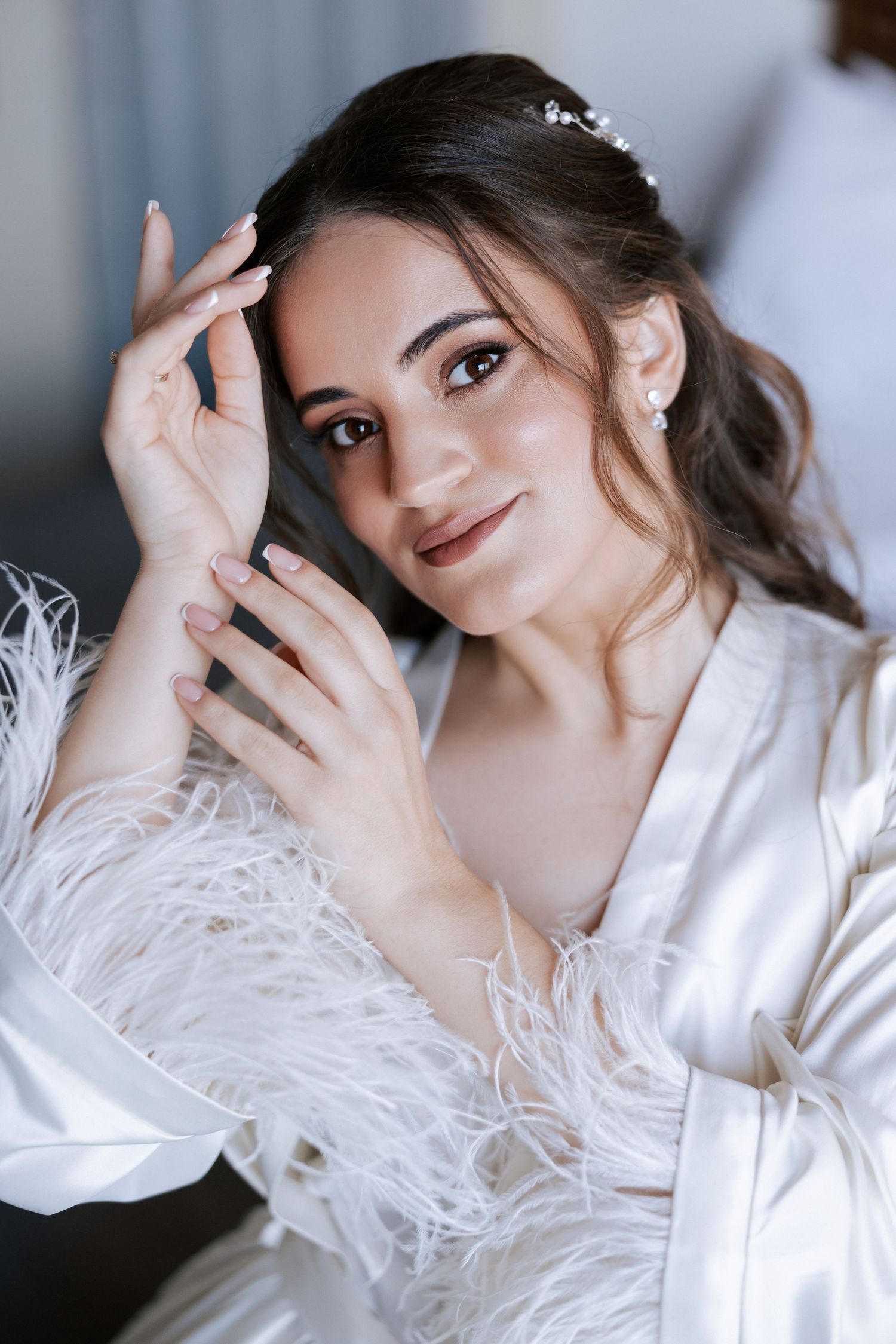 Portrait of someone in white silk robe with feather details preparing for a special occasion.