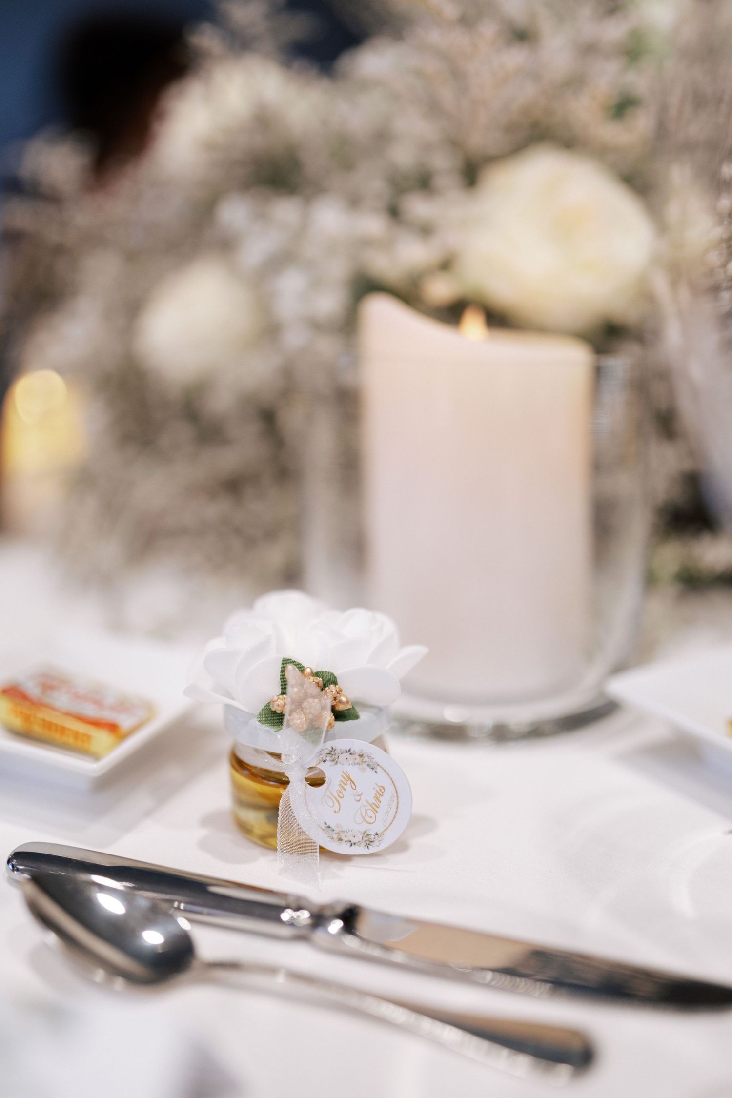 Elegant wedding favor and place setting with white candle and delicate floral accents.