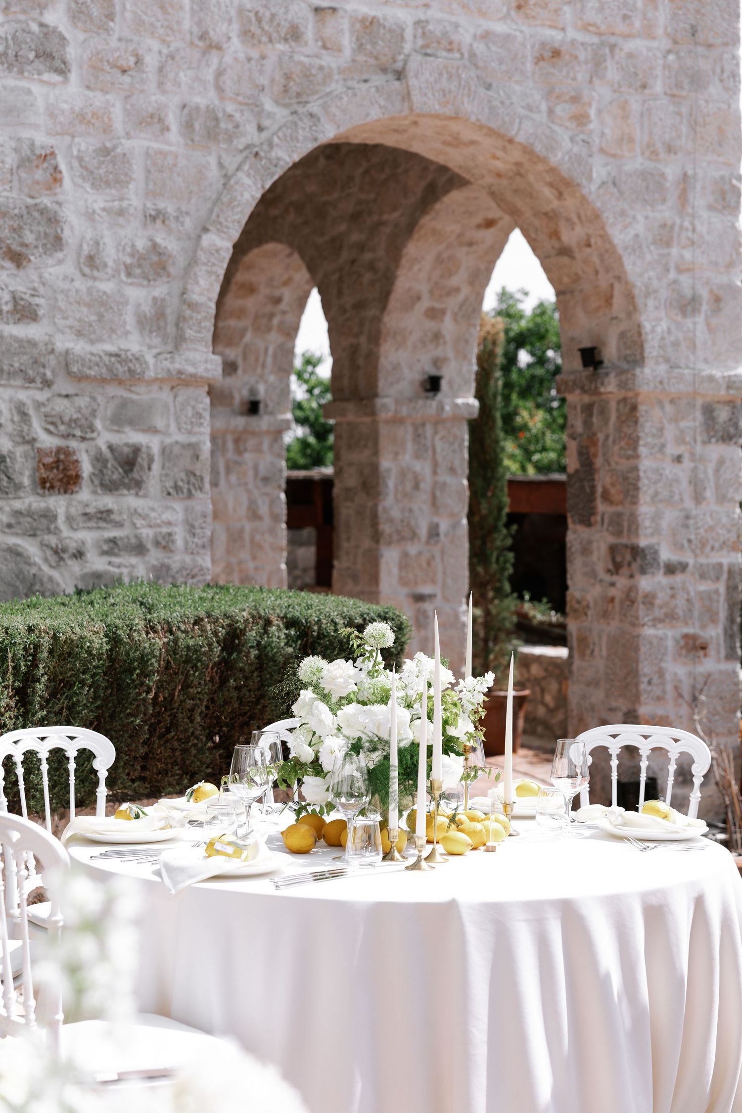 Elegant wedding reception tables with white linens set beneath stone arches in a rustic Mediterranean venue.