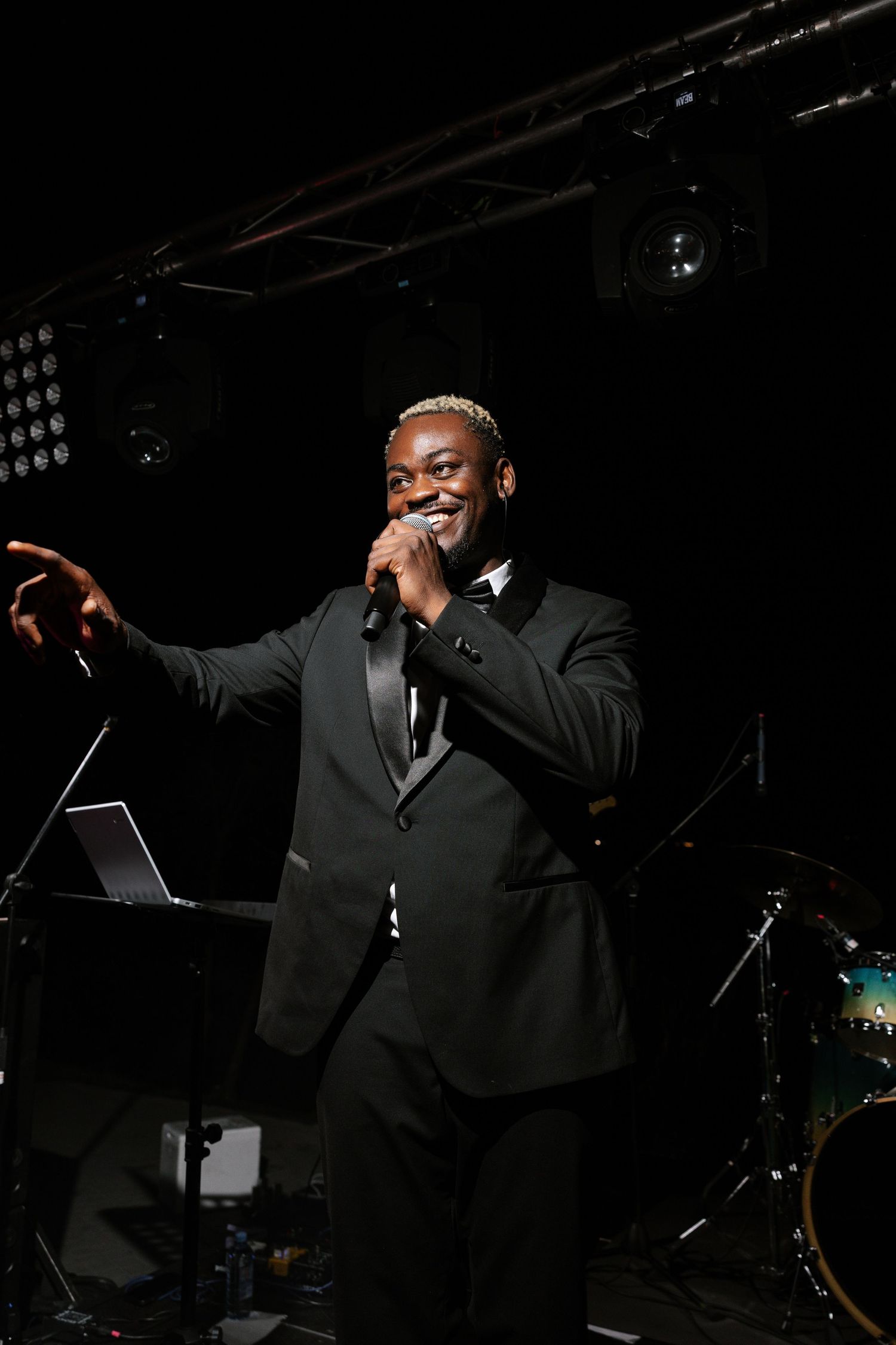 Performer in a black suit singing on stage with dramatic lighting.