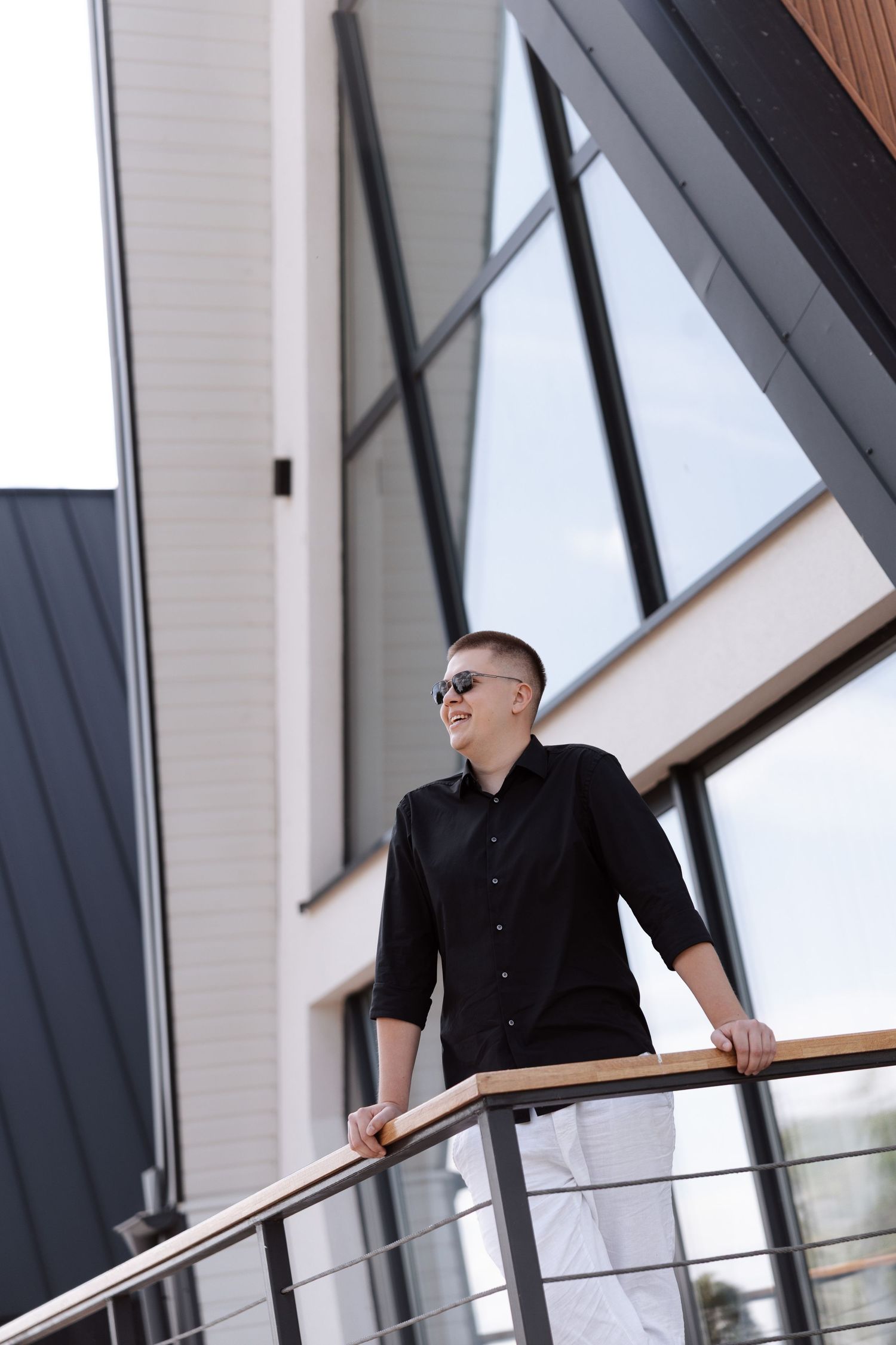 Person in black shirt leaning on modern architectural railing with geometric windows in background.
