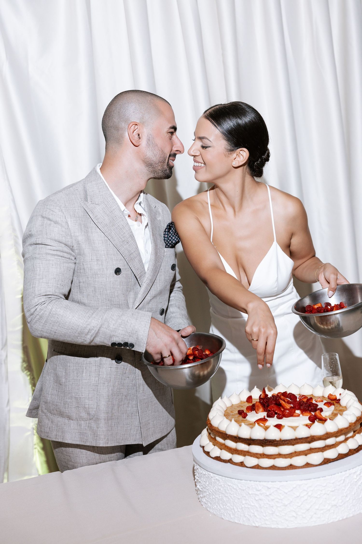 Newlywed couple shares sweet moments while cutting and feeding each other bites of their strawberry wedding cake.